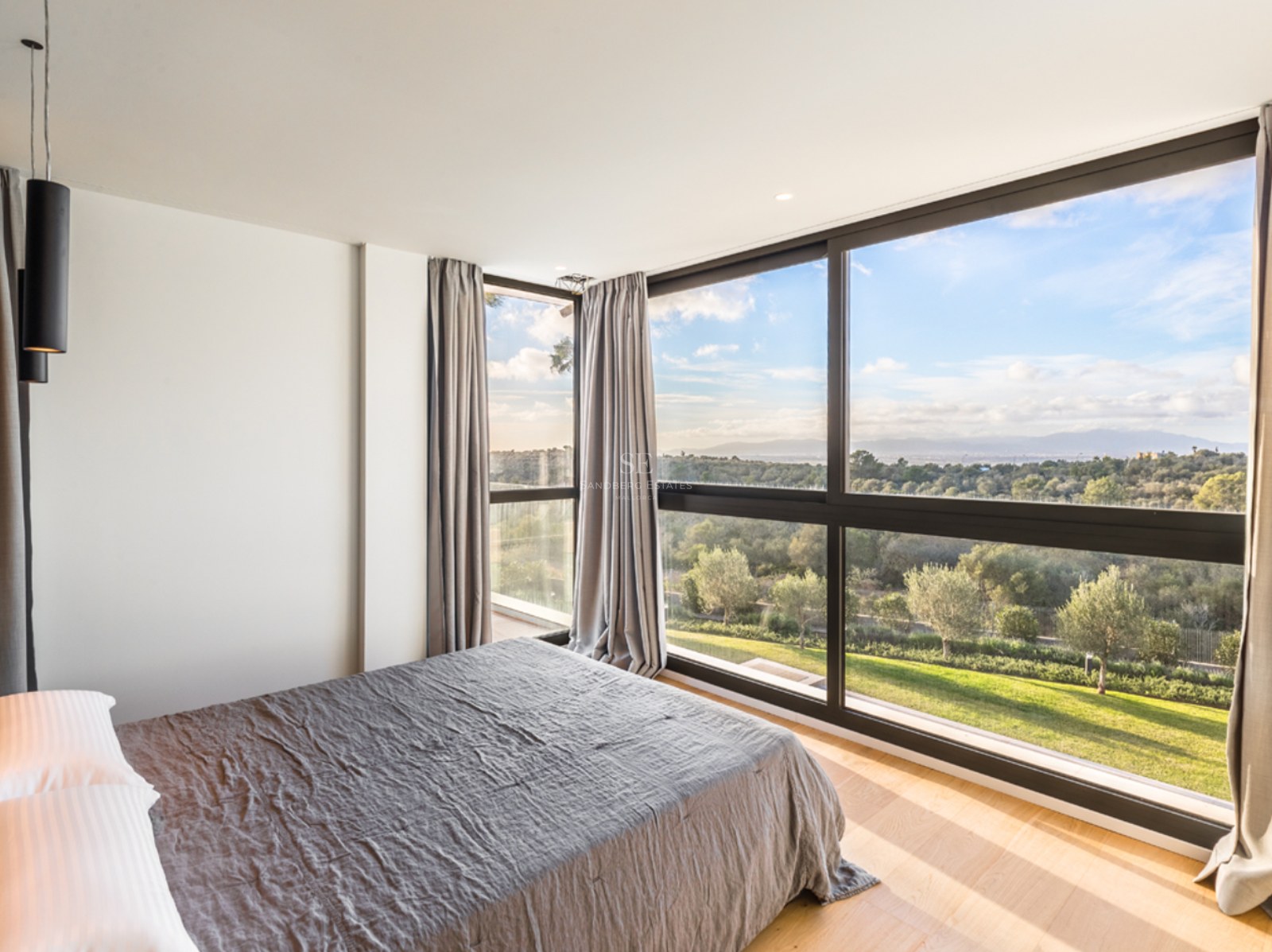 Chambre moderne avec de grandes baies vitrées donnant sur un paysage verdoyant et un ciel bleu.