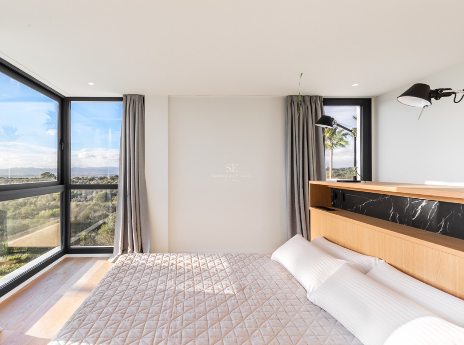 Chambre lumineuse avec tête de lit en chêne, accents de marbre noir et grandes fenêtres d'angle donnant sur la nature.