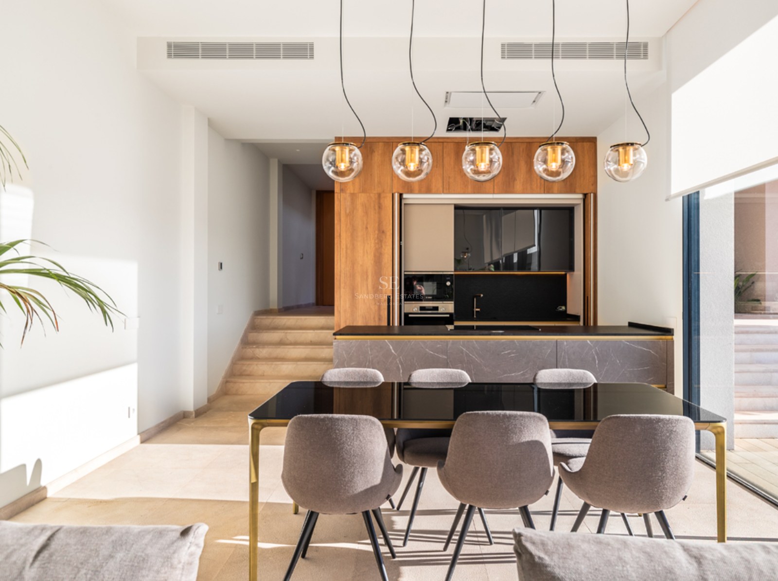 Cuisine contemporaine avec menuiserie en bois, îlot en pierre et table à manger noire sous cinq suspensions globes.