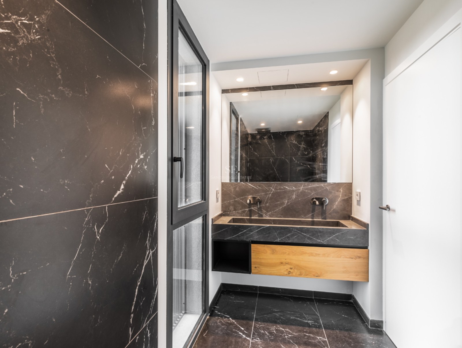 Salle de bain moderne avec murs et sol en marbre noir, lavabo intégré en pierre et meuble sous-vasque en bois.