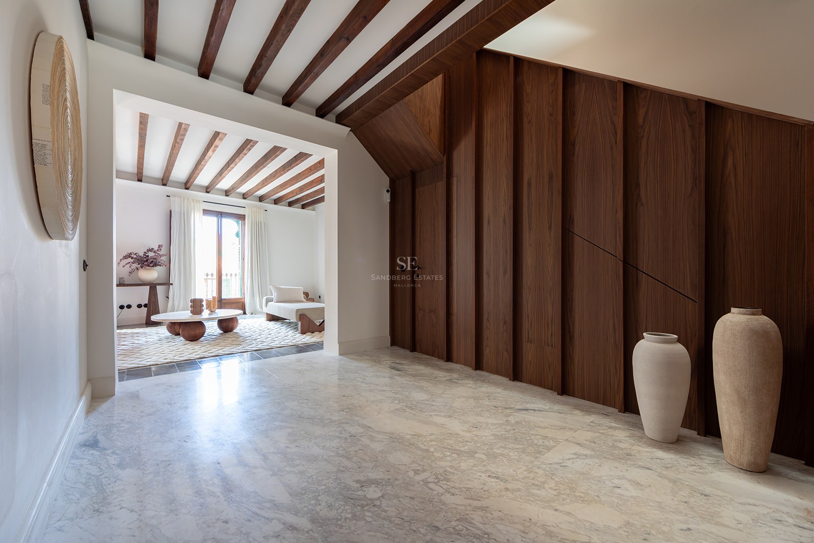 Vestíbulo de lujo con suelo de mármol, panelado de madera oscura y vigas de madera que conecta con el salón.