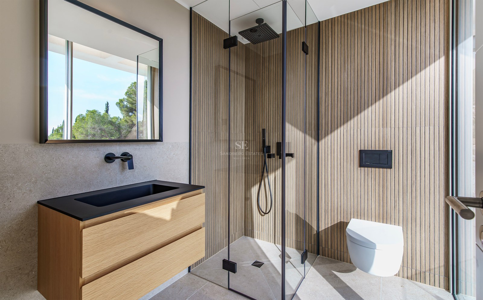 Salle de bain moderne avec murs en lattes de bois, douche en verre, vasque noire et lumière naturelle.