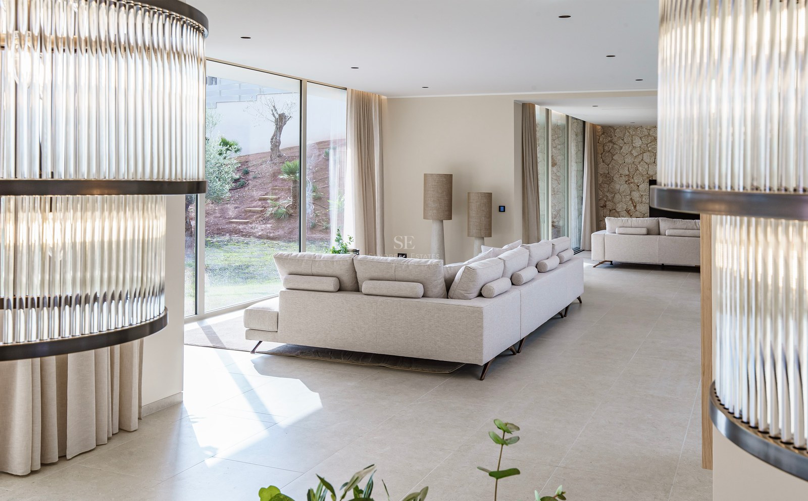 Grand salon moderne avec canapé crème, larges baies vitrées sur le jardin et mur d'accent en pierre.
