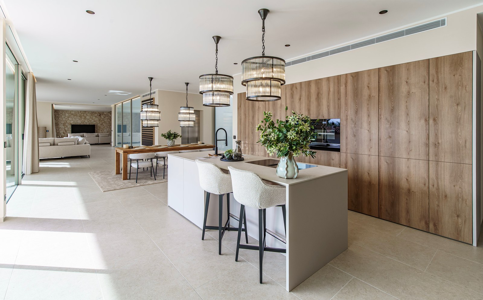 Cuisine moderne avec un grand îlot, tabourets blancs, suspensions design et armoires en bois dans un espace ouvert.