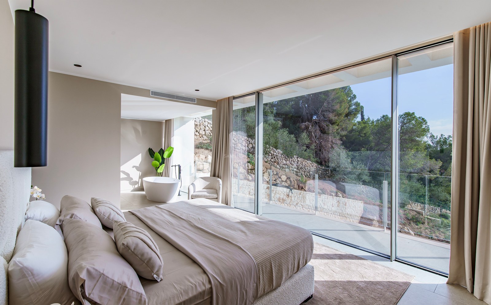 Chambre moderne avec baies vitrées, grand lit aux tons neutres et baignoire îlot avec vue sur le jardin.