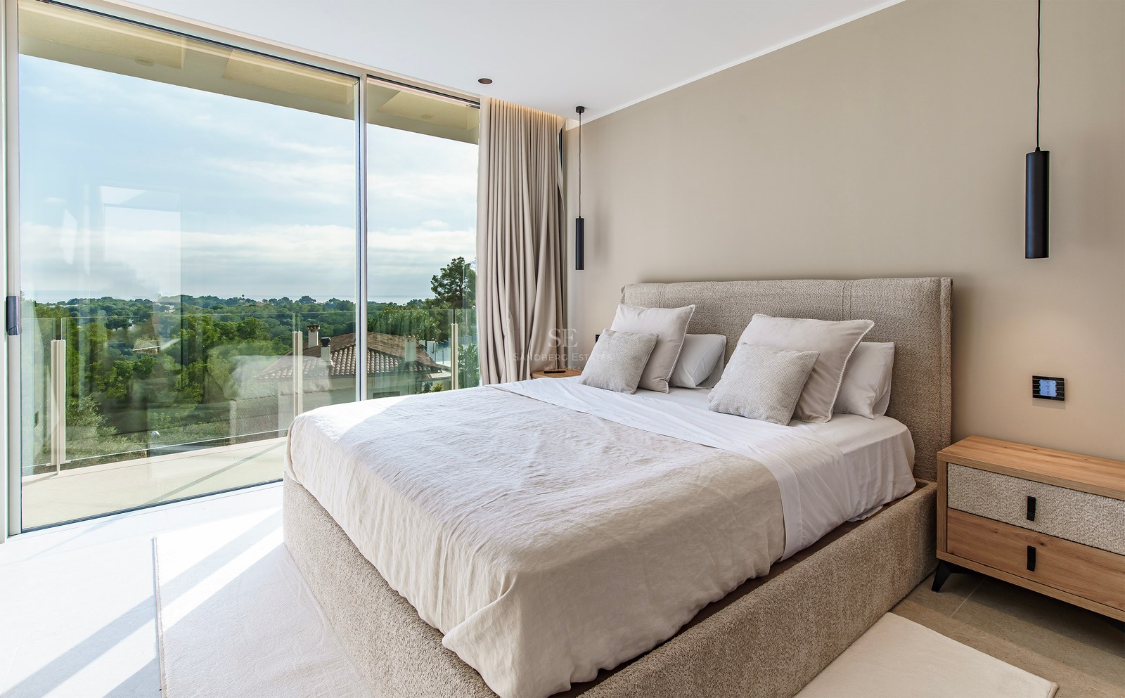 Chambre parentale moderne avec baies vitrées du sol au plafond donnant sur un paysage verdoyant et grand lit neutre.