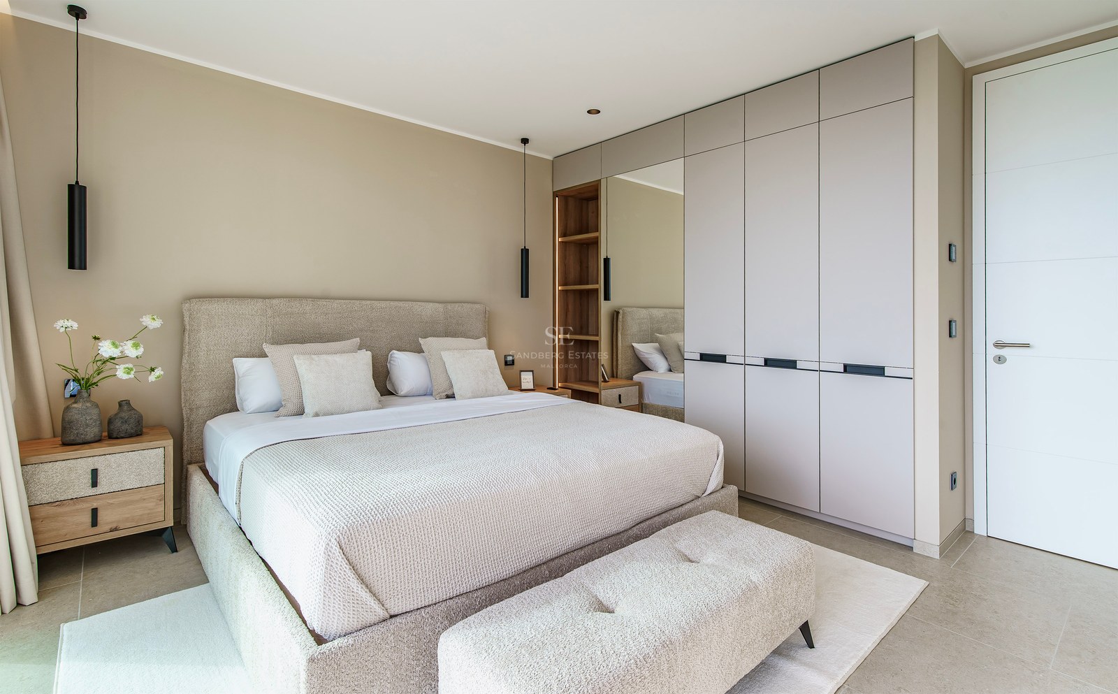 Chambre moderne avec un grand lit rembourré beige, des placards intégrés et des suspensions noires élégantes.
