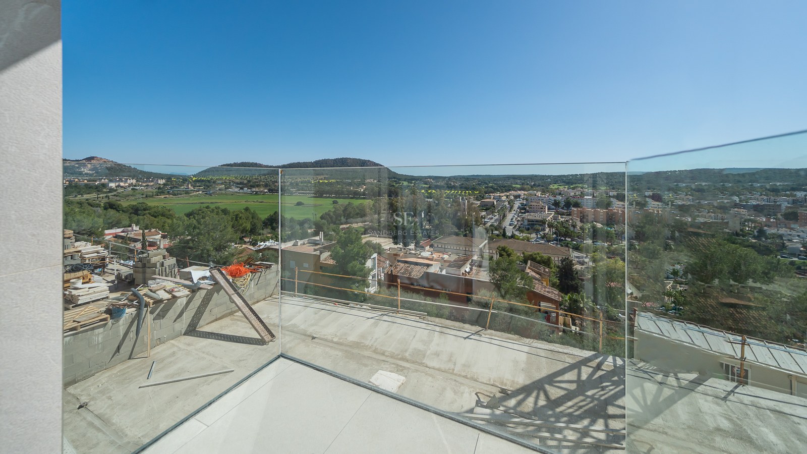 Terrasse en cours de finition avec garde-corps en verre surplombant une vallée et un village méditerranéen.