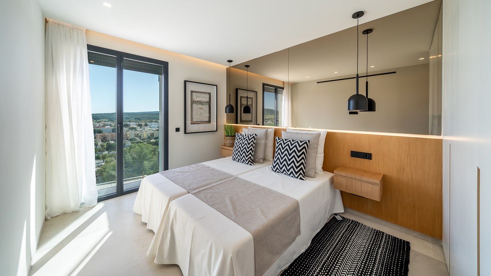 Chambre moderne avec lit double, tête de lit en bois, grand miroir mural et vue dégagée sur le paysage.