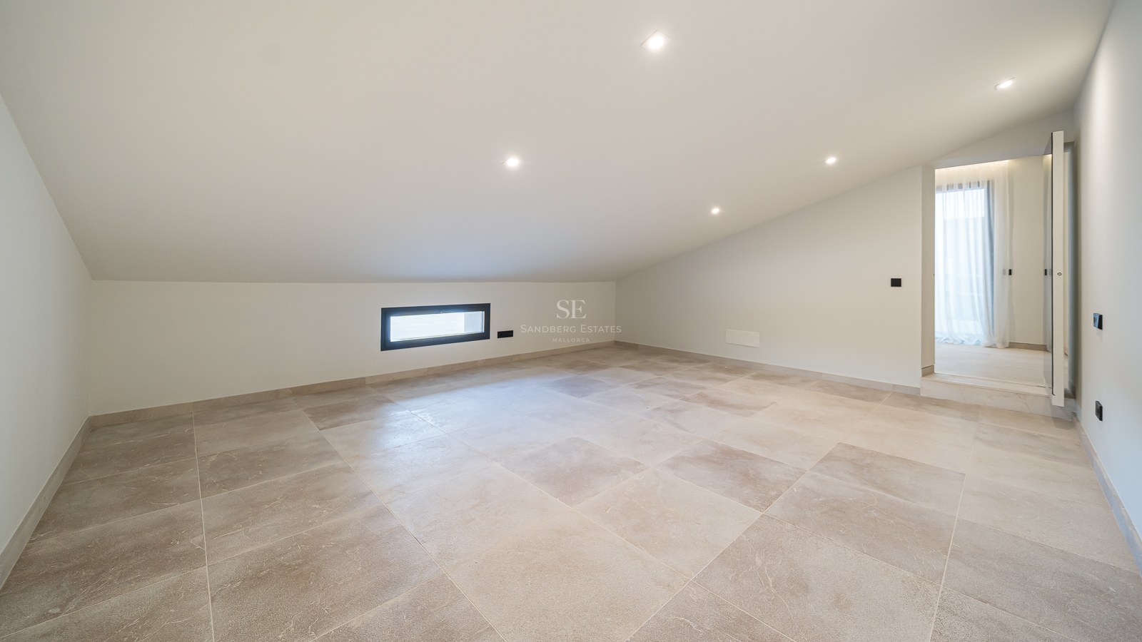 Pièce mansardée vide avec carrelage beige, plafond blanc incliné et spots encastrés.