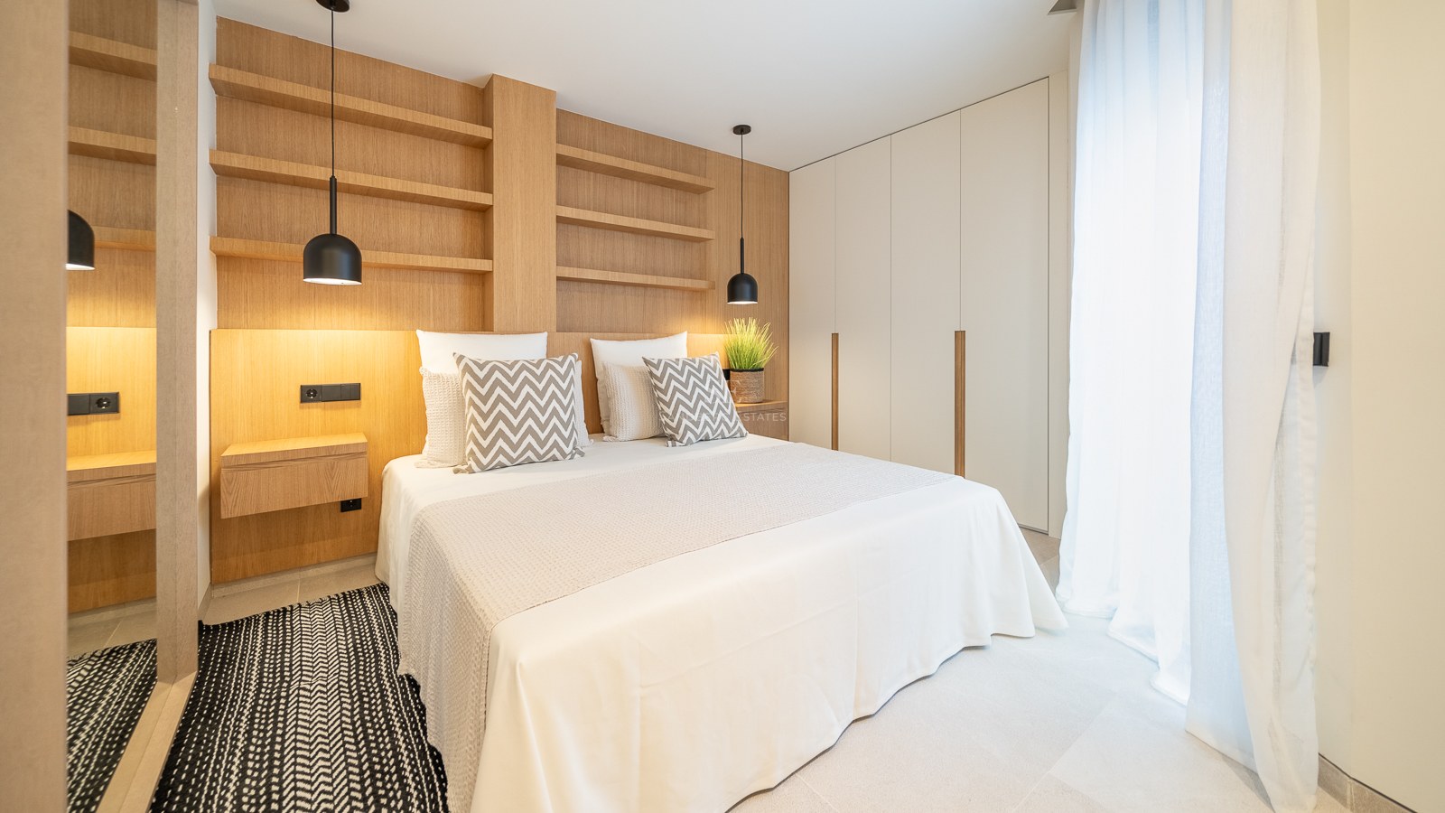 Chambre moderne avec mur en chêne clair, étagères intégrées, suspensions noires et grandes armoires blanches.