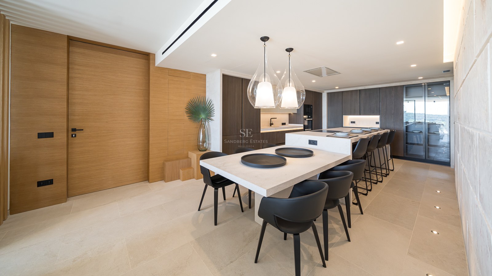 Cuisine moderne avec un grand îlot en pierre, boiseries en chêne, chaises en cuir noir et suspensions en verre.