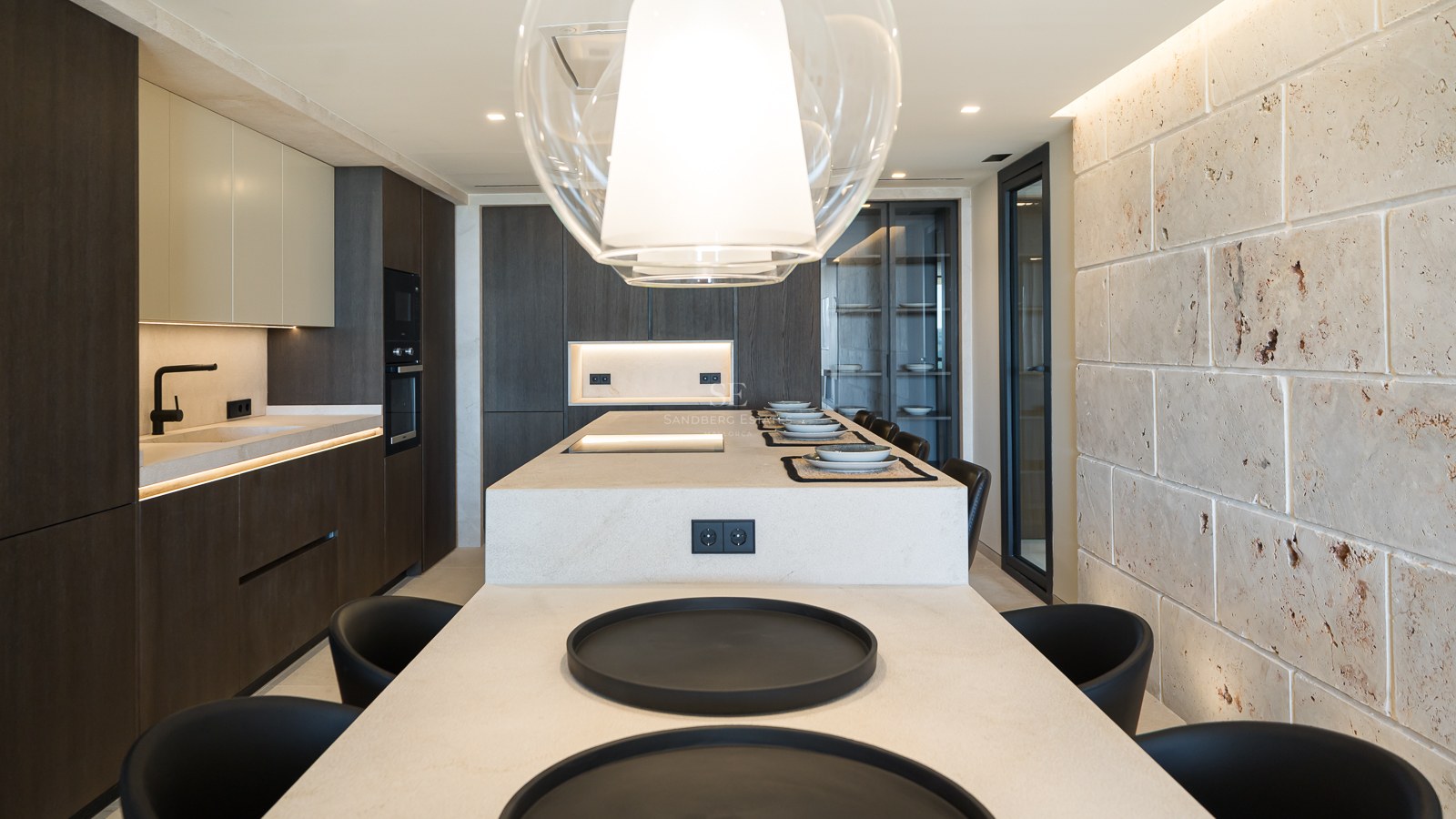 Cuisine contemporaine avec îlot en pierre, armoires en bois sombre et mur en pierre naturelle texturée.