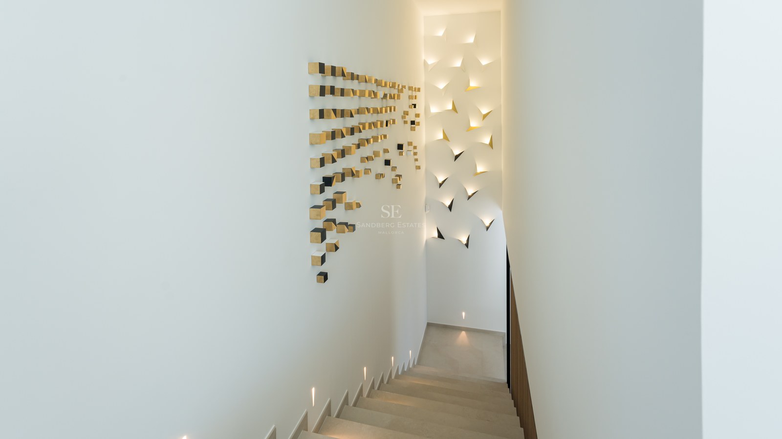 Modern minimalist staircase featuring integrated LED wall lighting and gold geometric art on white walls.