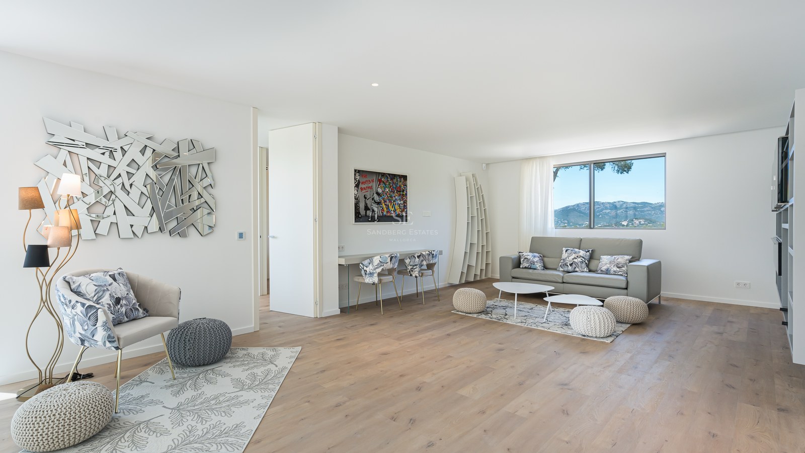Bright modern living room with oak floors, grey sofa, designer mirror, and a window framing mountain scenery.