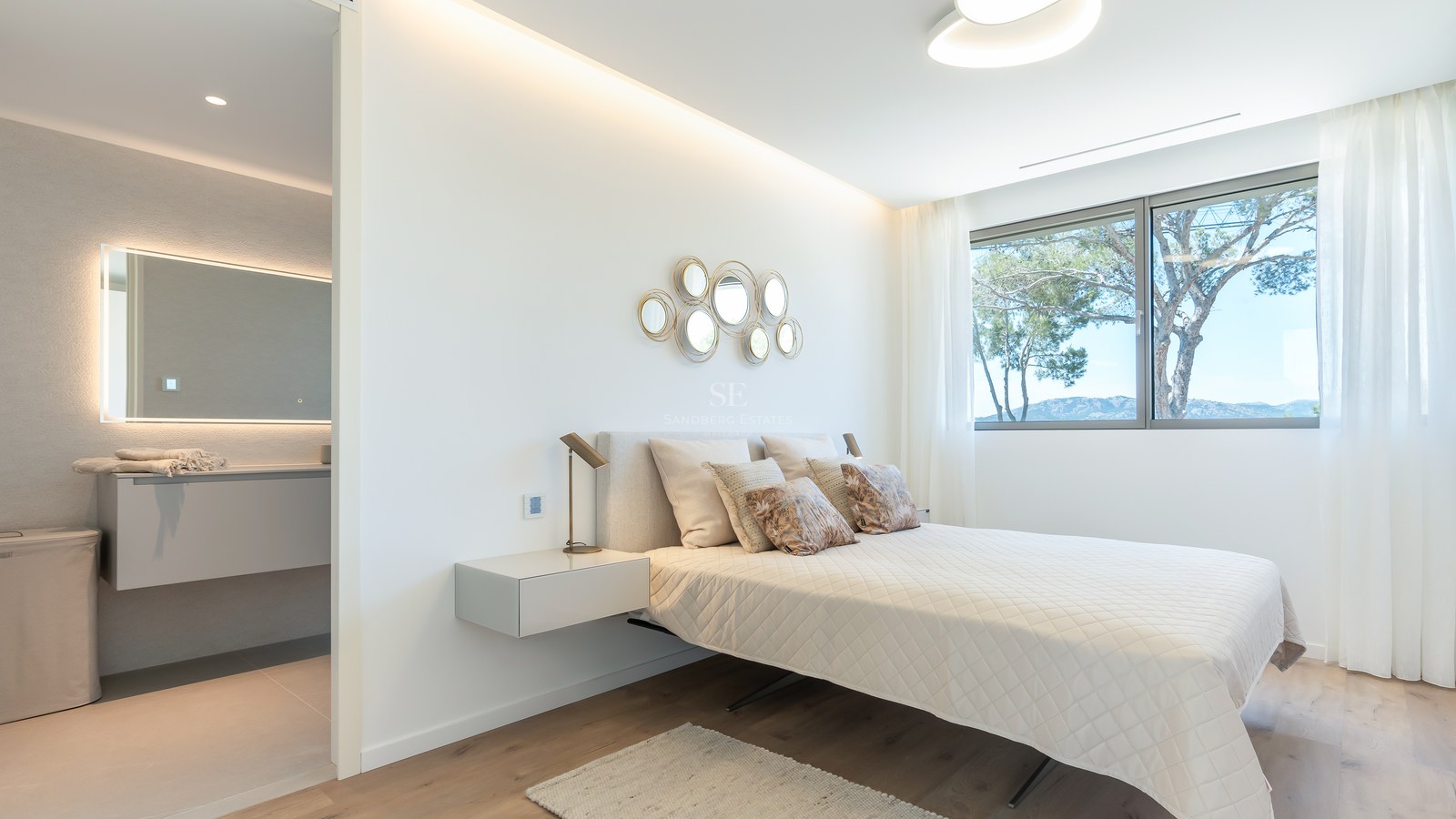 Bright bedroom featuring a queen bed, wooden floors, large windows with mountain views, and an ensuite bathroom.