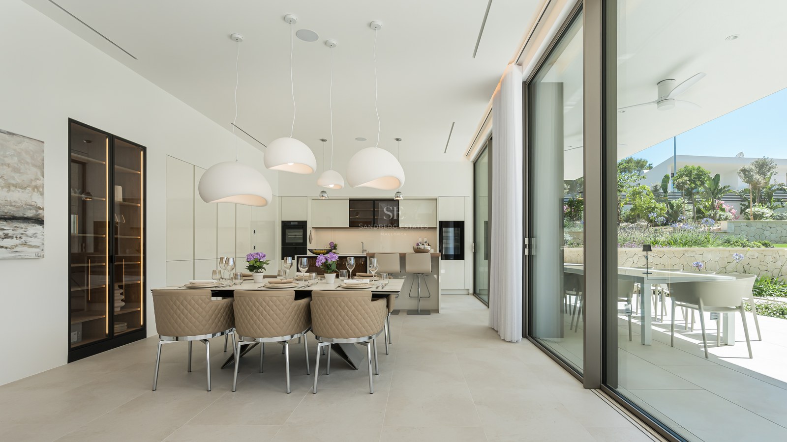 Modern dining area with quilted beige chairs, designer pendant lights, and floor-to-ceiling glass doors to the terrace.