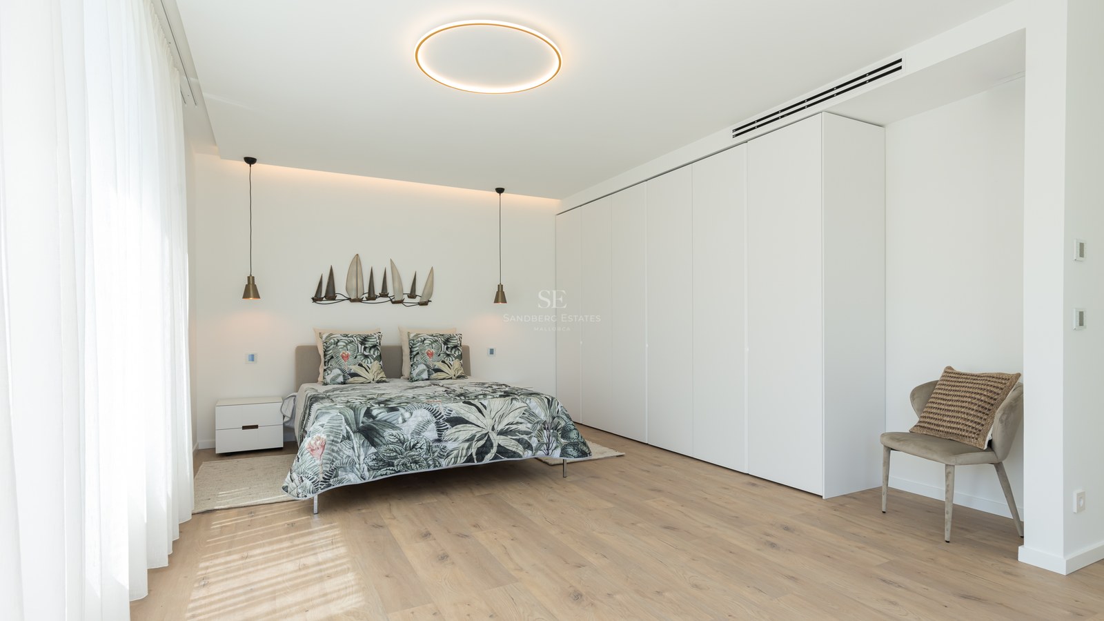 Bright contemporary bedroom featuring light wood floors, a large white wardrobe wall, and minimalist circular lighting.
