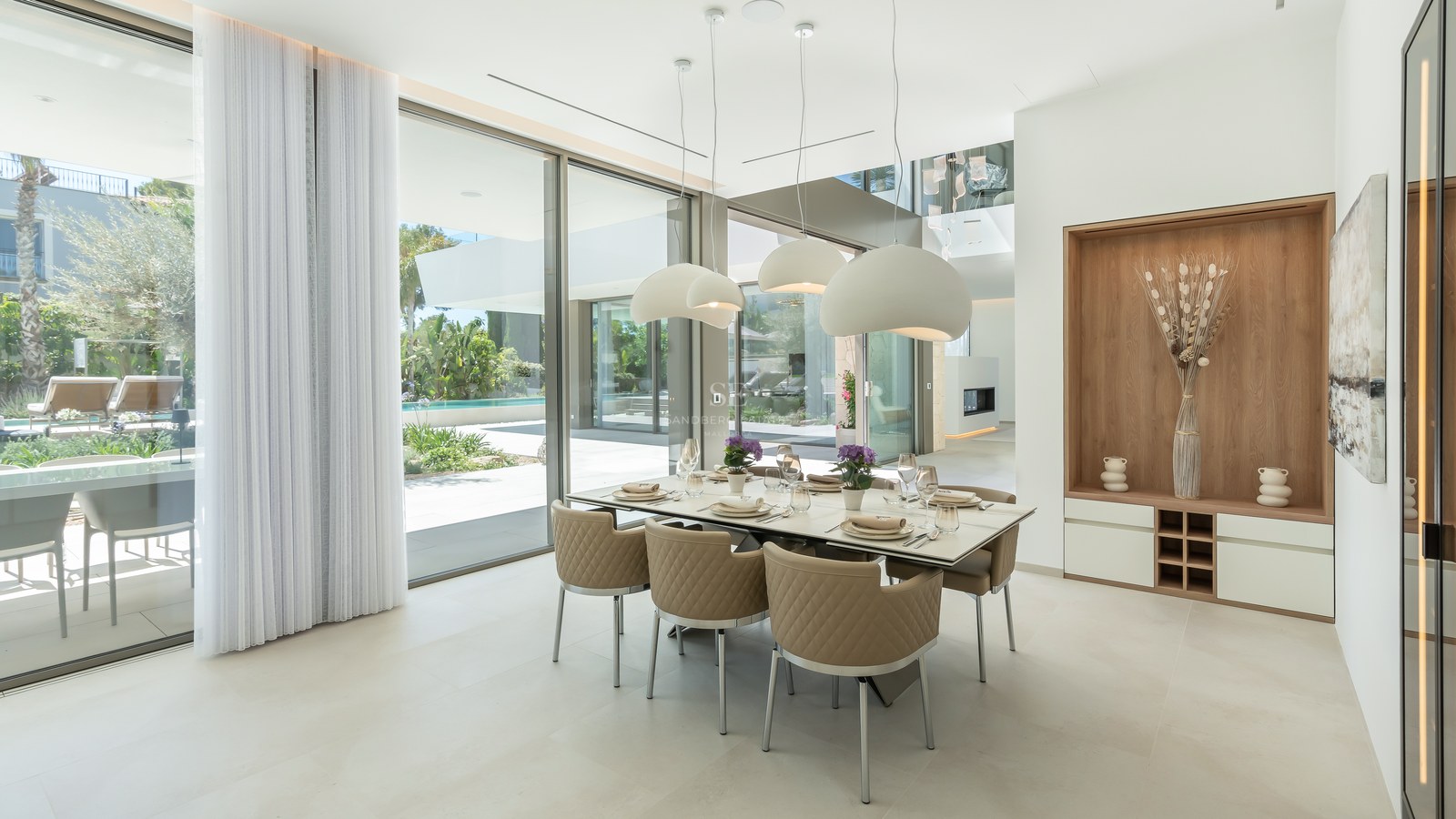 Modern dining room featuring an eight-person table, beige quilted chairs, and floor-to-ceiling glass doors overlooking a pool.