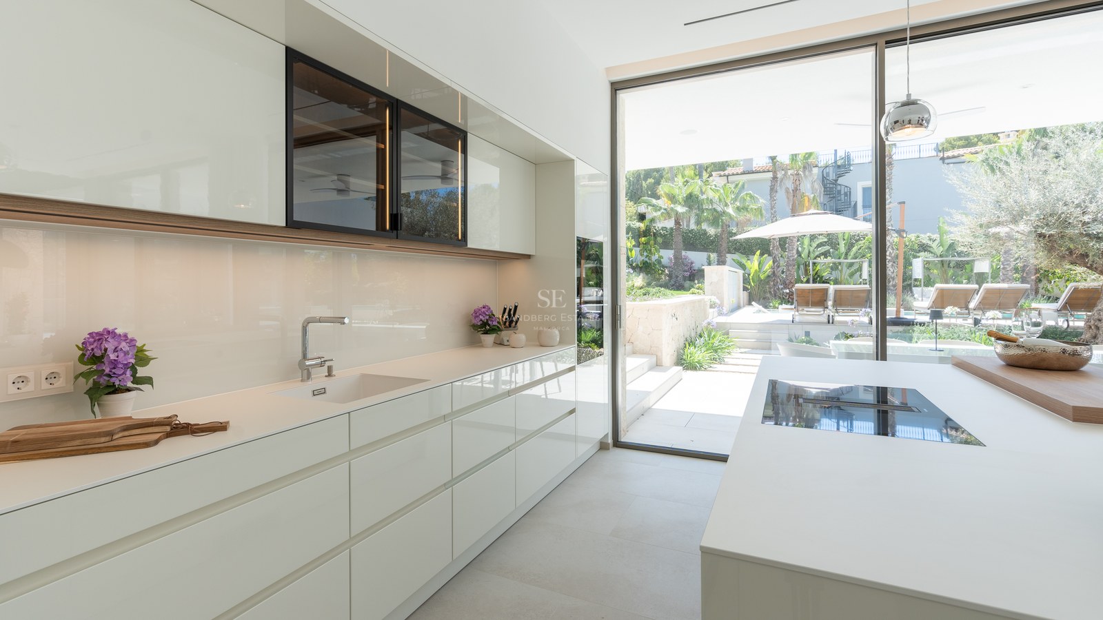 Contemporary white kitchen with high-gloss cabinets and large sliding glass doors opening to a Mediterranean garden.