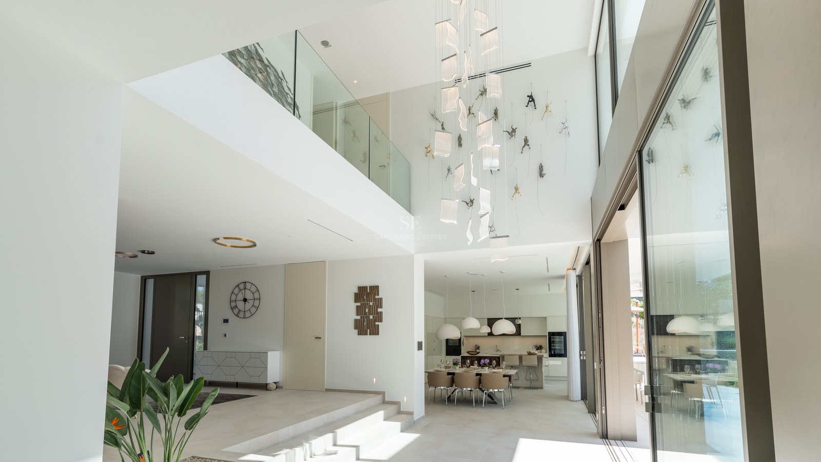 Bright double-height living space with glass balustrades, designer pendant lighting, and floor-to-ceiling windows.
