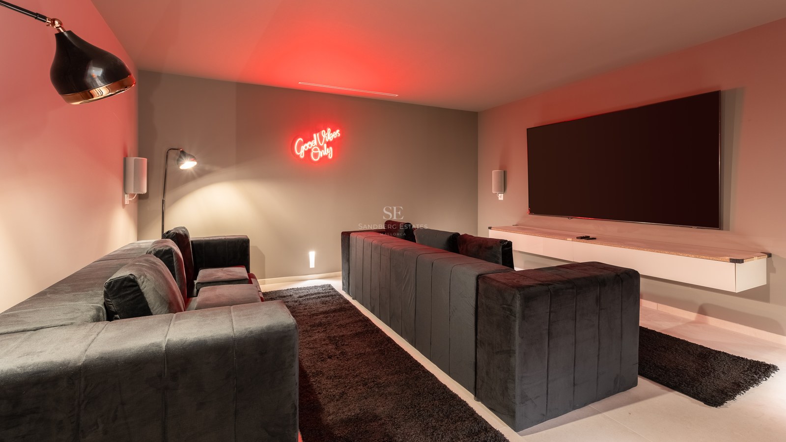 Home cinema room featuring deep charcoal velvet sofas, a large wall-mounted screen, and red neon wall art.