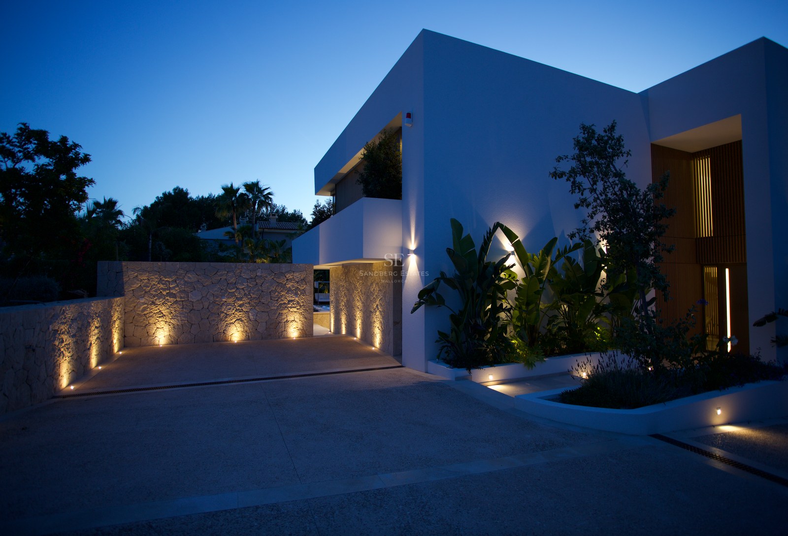 Modern white villa exterior featuring natural stone walls and integrated uplighting at dusk.
