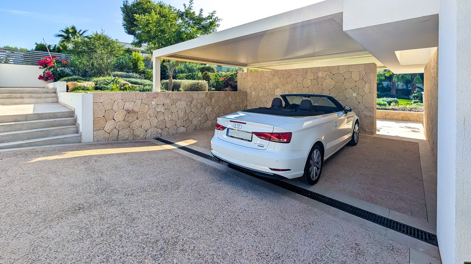White convertible parked in a modern carport featuring natural stone walls and aggregate driveway beside stone stairs.