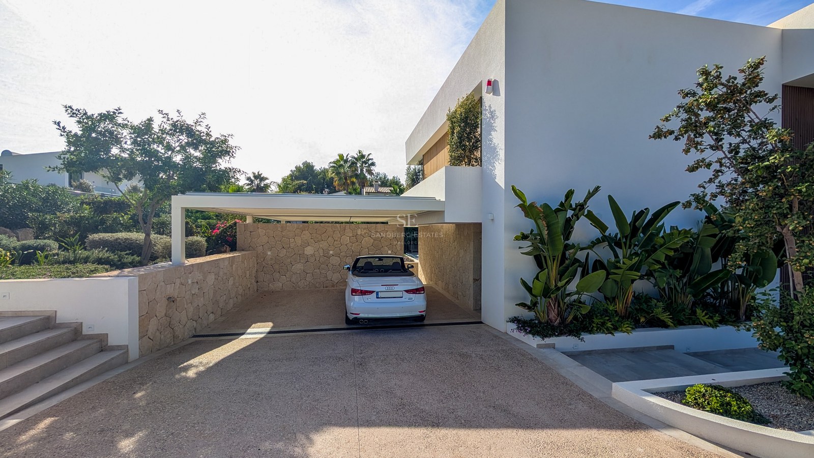 White convertible parked in a modern covered carport featuring natural stone walls and tropical landscaping.