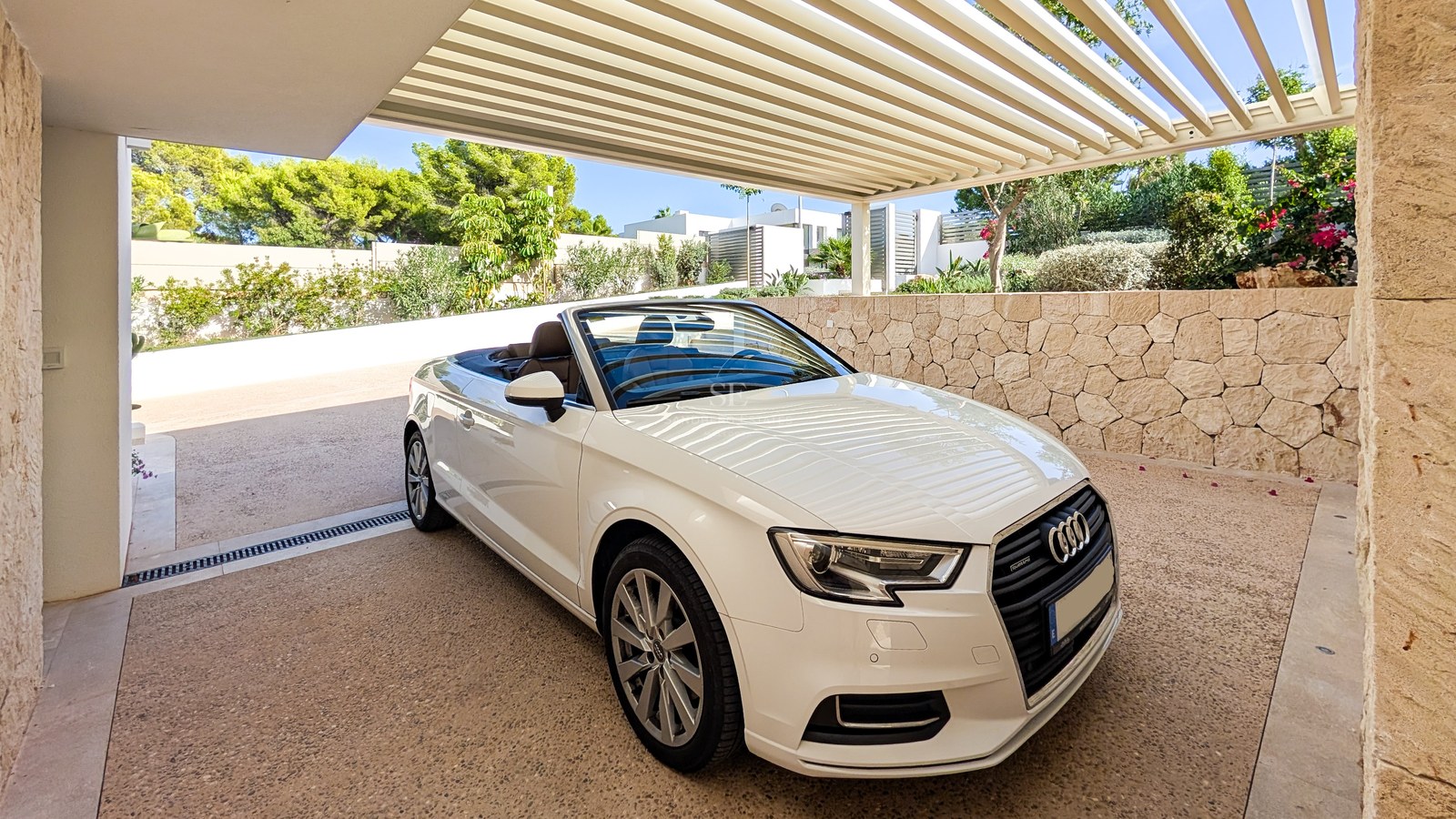 A white convertible car parked in a modern carport with a slatted roof and natural stone feature walls.
