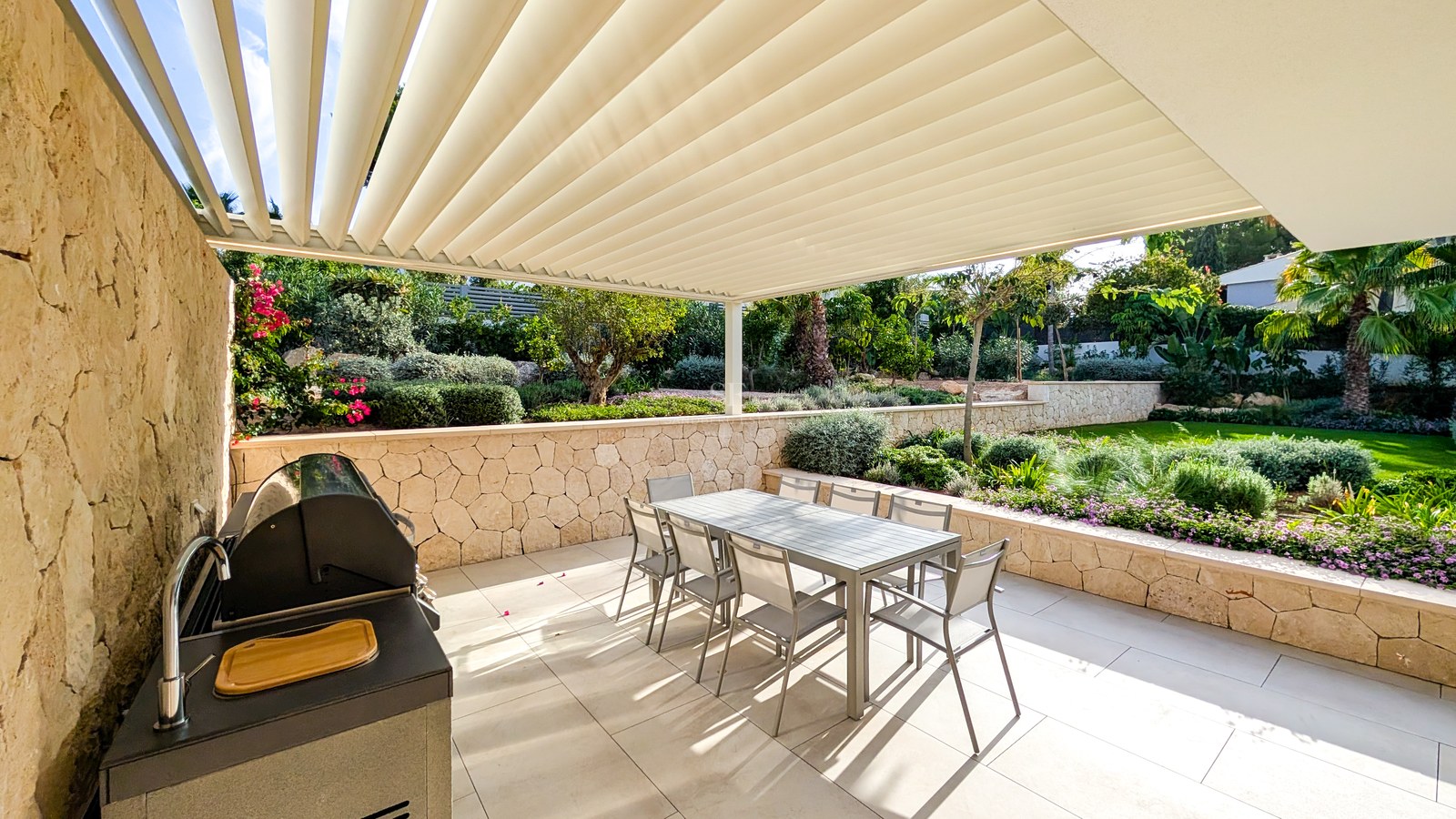 Modern terrace featuring a bioclimatic pergola, dining set for six, integrated BBQ, and a lush Mediterranean garden.