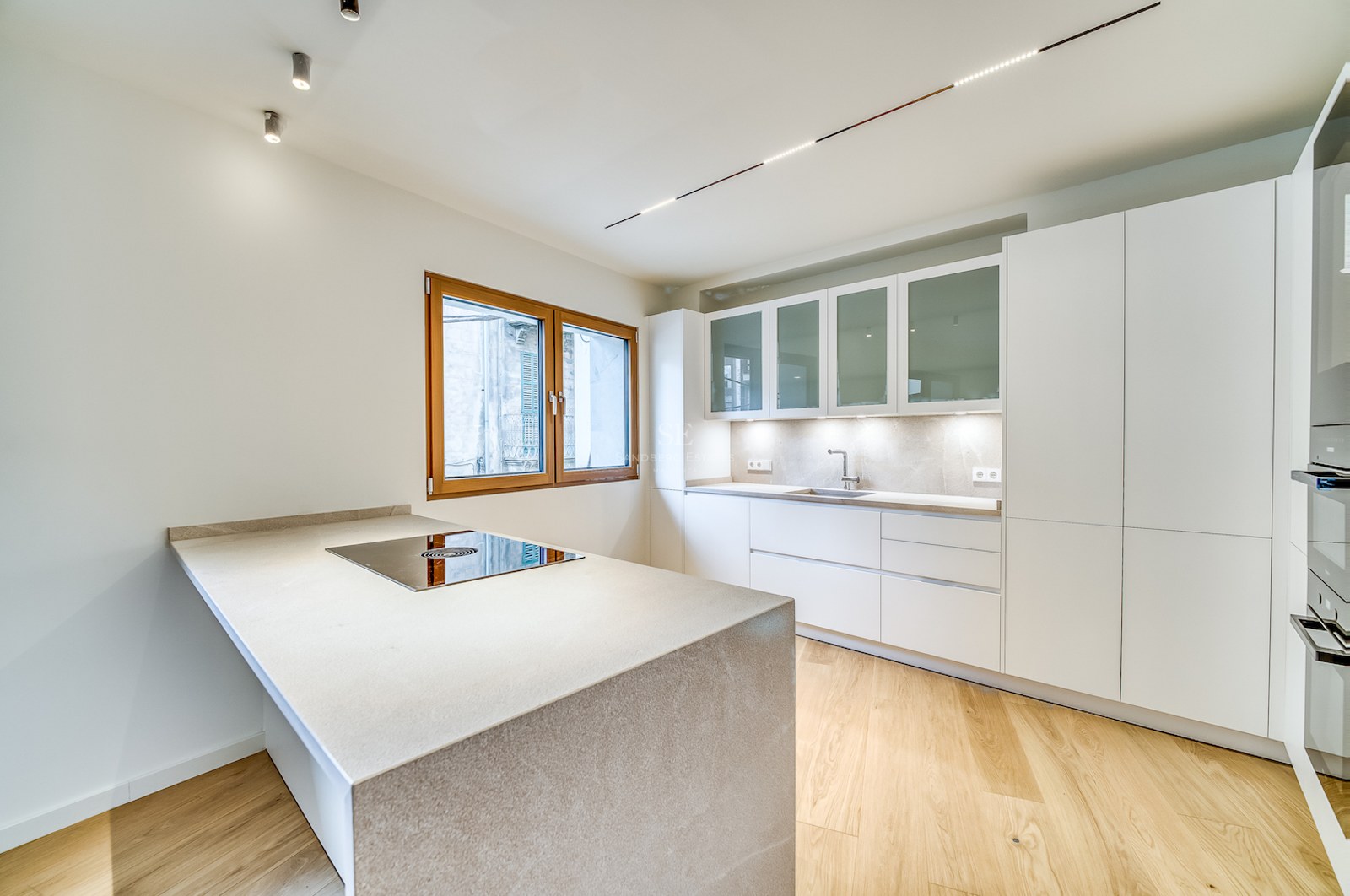 Cuisine moderne lumineuse avec îlot en pierre, plaque intégrée, armoires blanches et parquet en chêne.