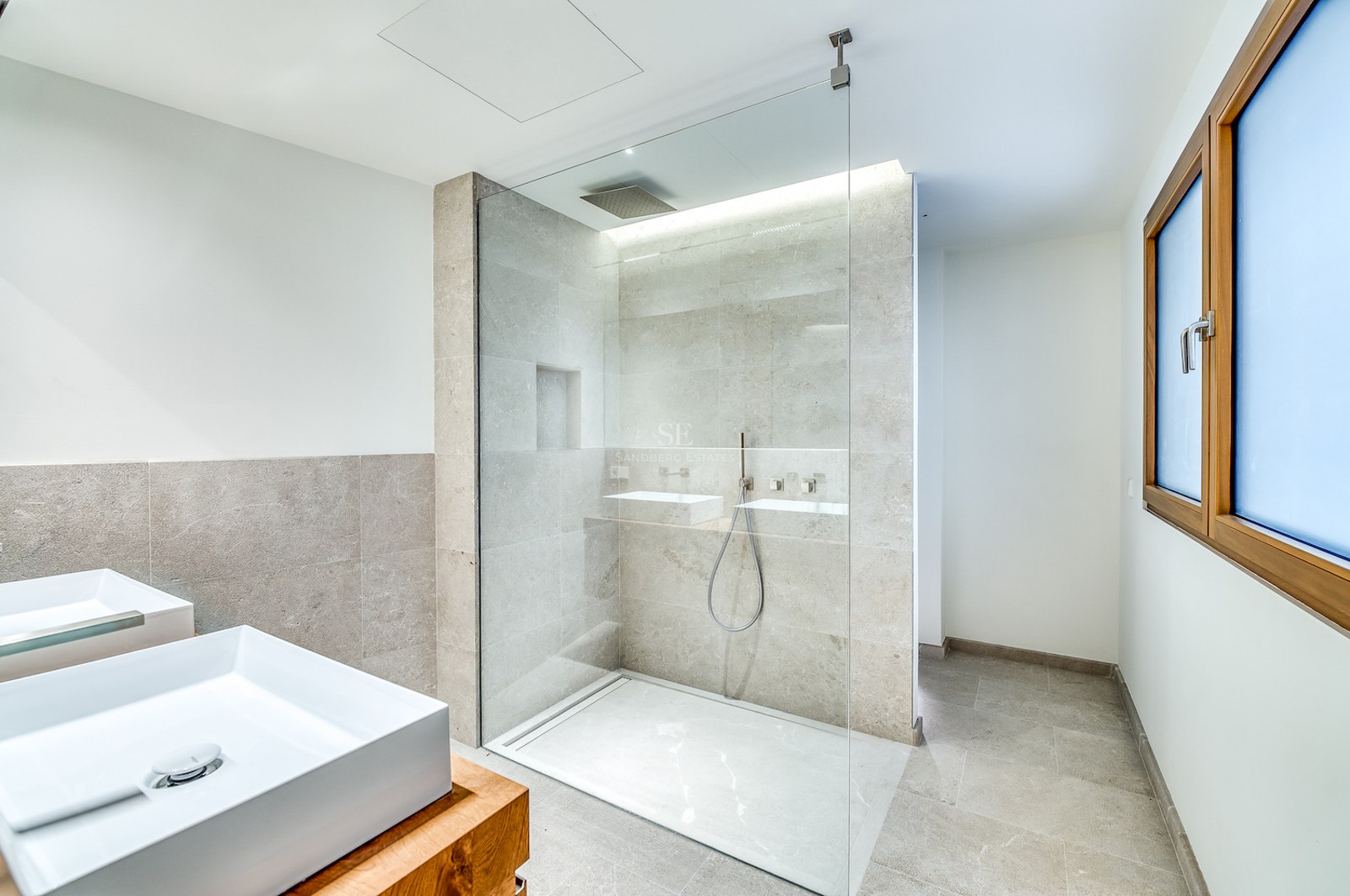 Salle de bain moderne avec douche vitrée, carrelage en pierre naturelle, double vasque et finitions en bois.