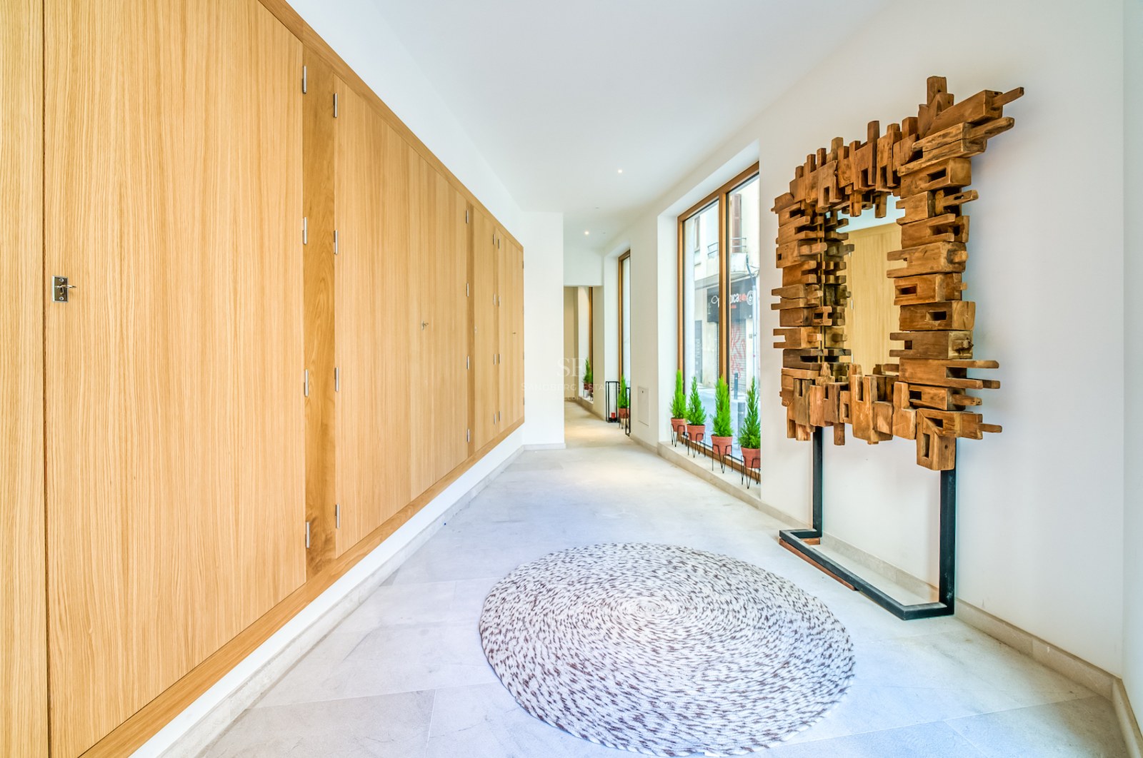 Couloir lumineux avec placards en chêne du sol au plafond, un miroir sculptural en bois et sol en pierre claire.