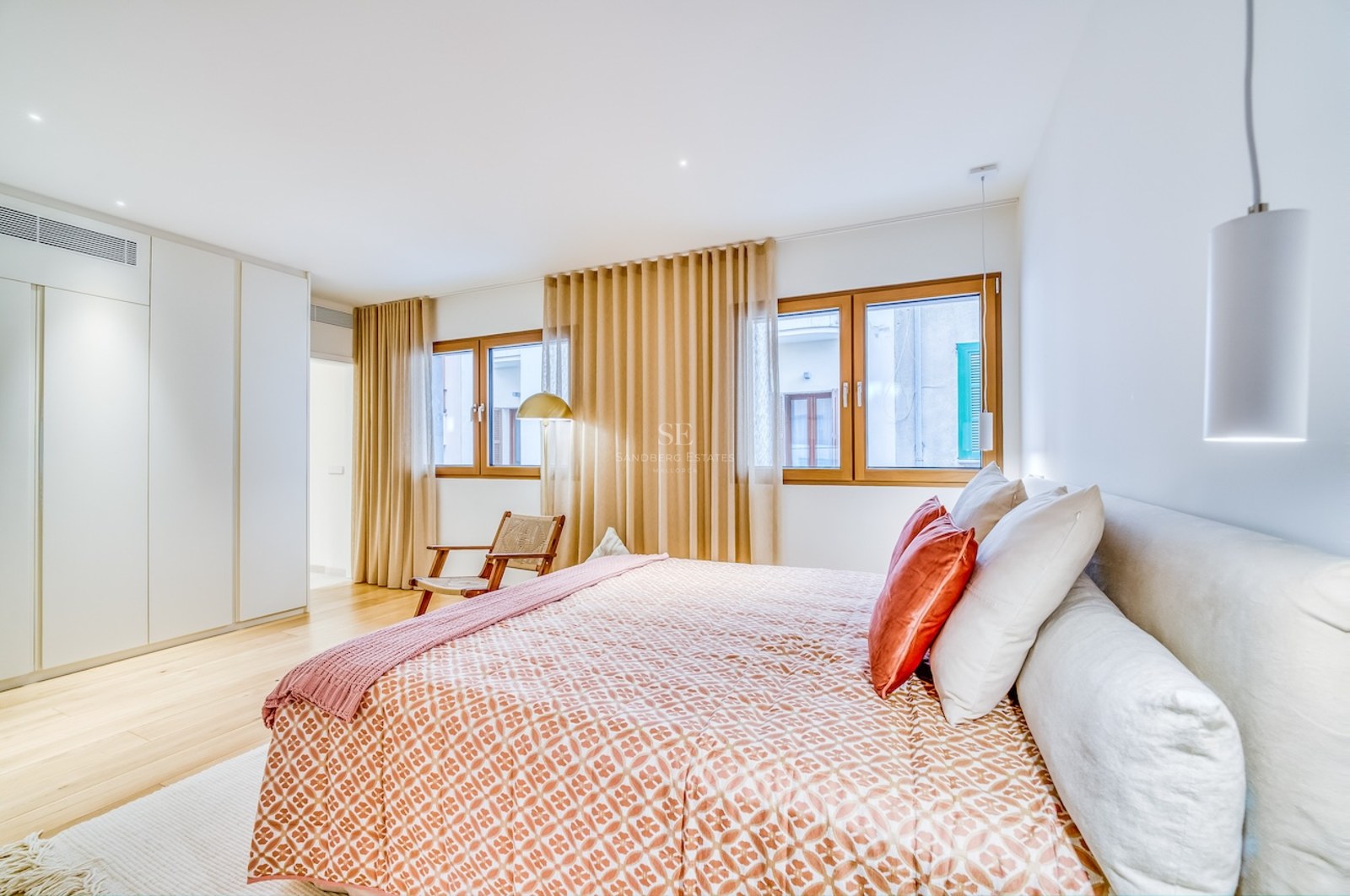 Chambre lumineuse avec grand lit, parquet en bois, placards intégrés blancs et menuiseries en bois.