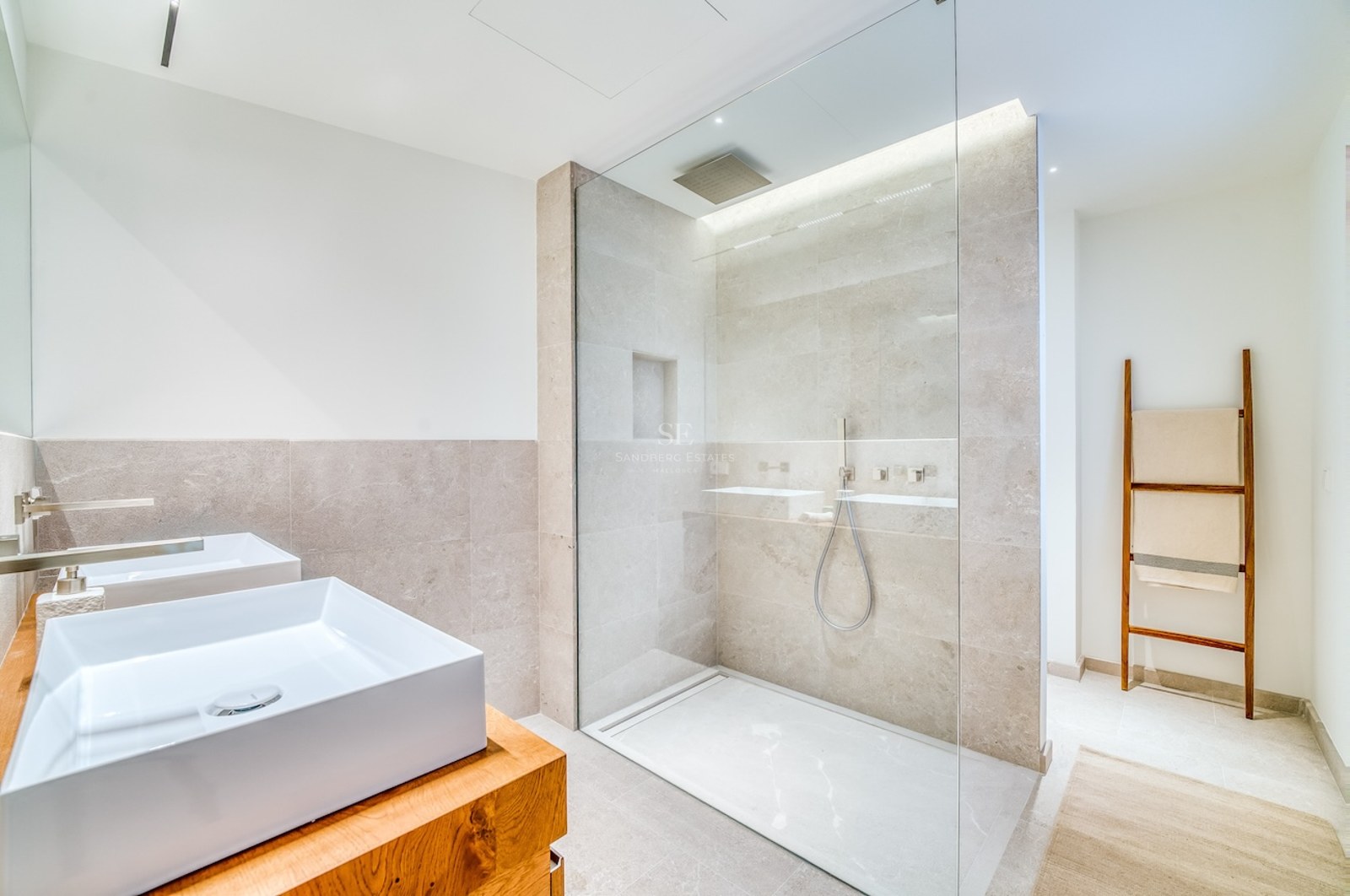 Salle de bains lumineuse avec deux vasques sur meuble en bois et une grande douche vitrée avec carrelage en pierre.