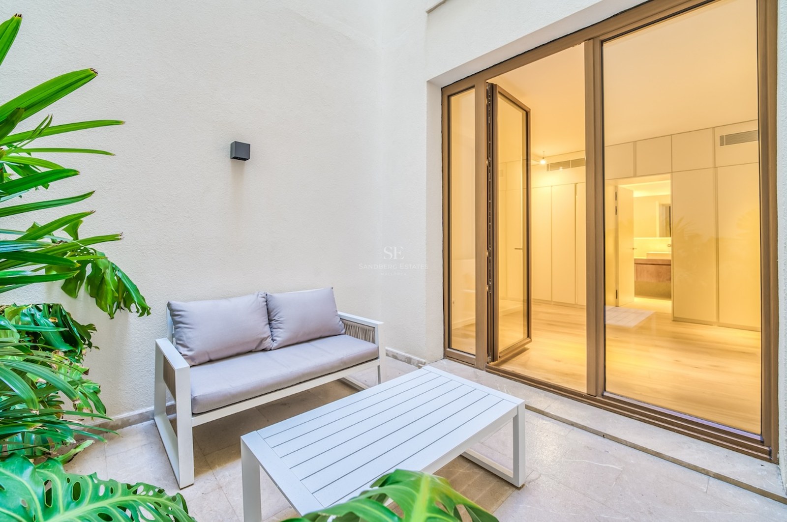 Petite terrasse privée avec mobilier moderne et baies vitrées menant à une chambre de maître contemporaine.