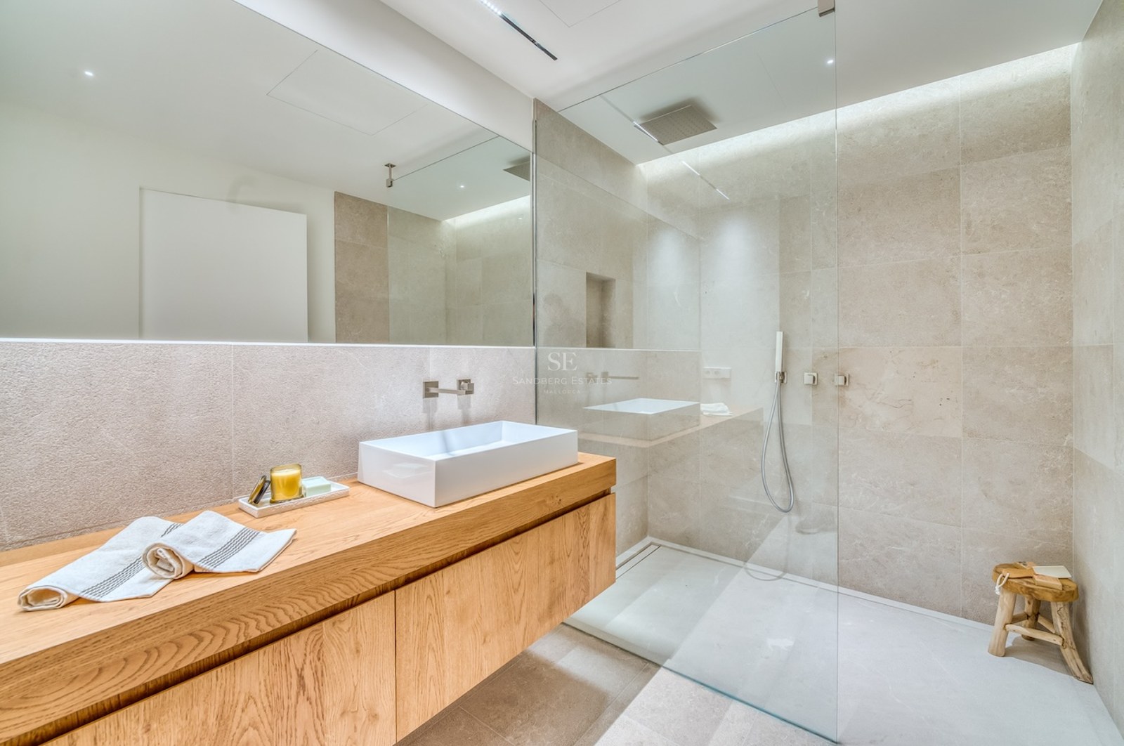 Salle de bain moderne avec meuble en chêne, vasque blanche et douche vitrée aux murs en pierre.