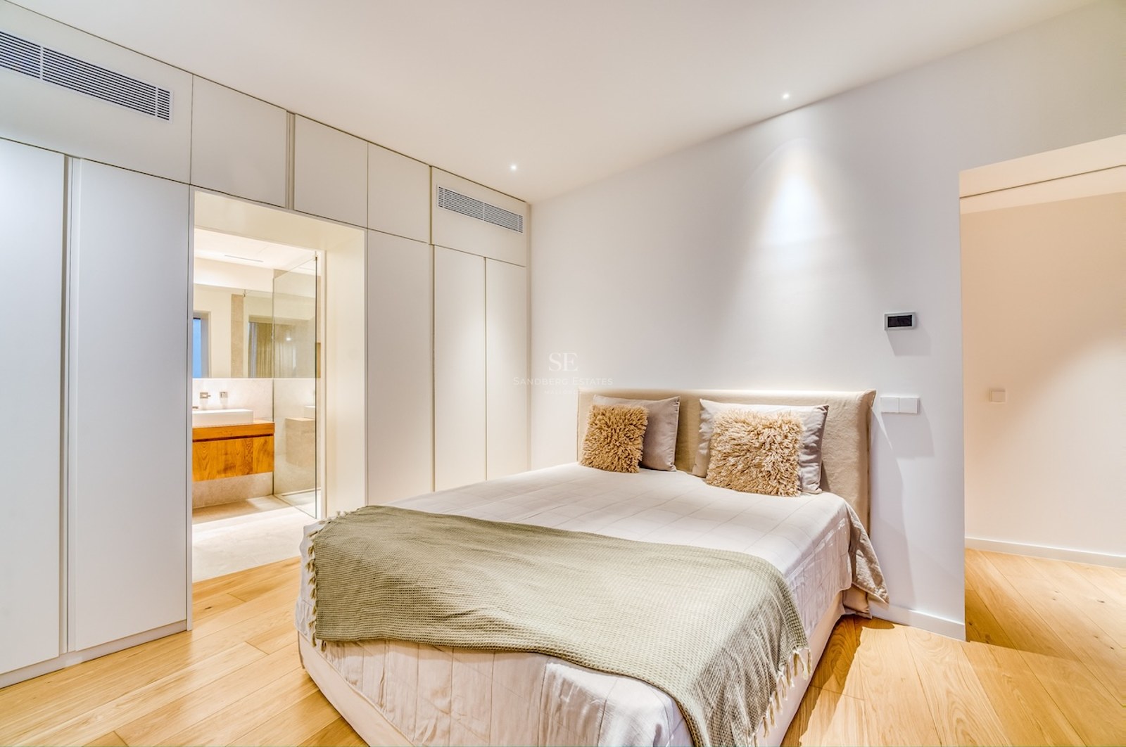 Chambre moderne avec lit double, placards intégrés blancs, parquet en chêne et vue sur la salle de bain en suite.