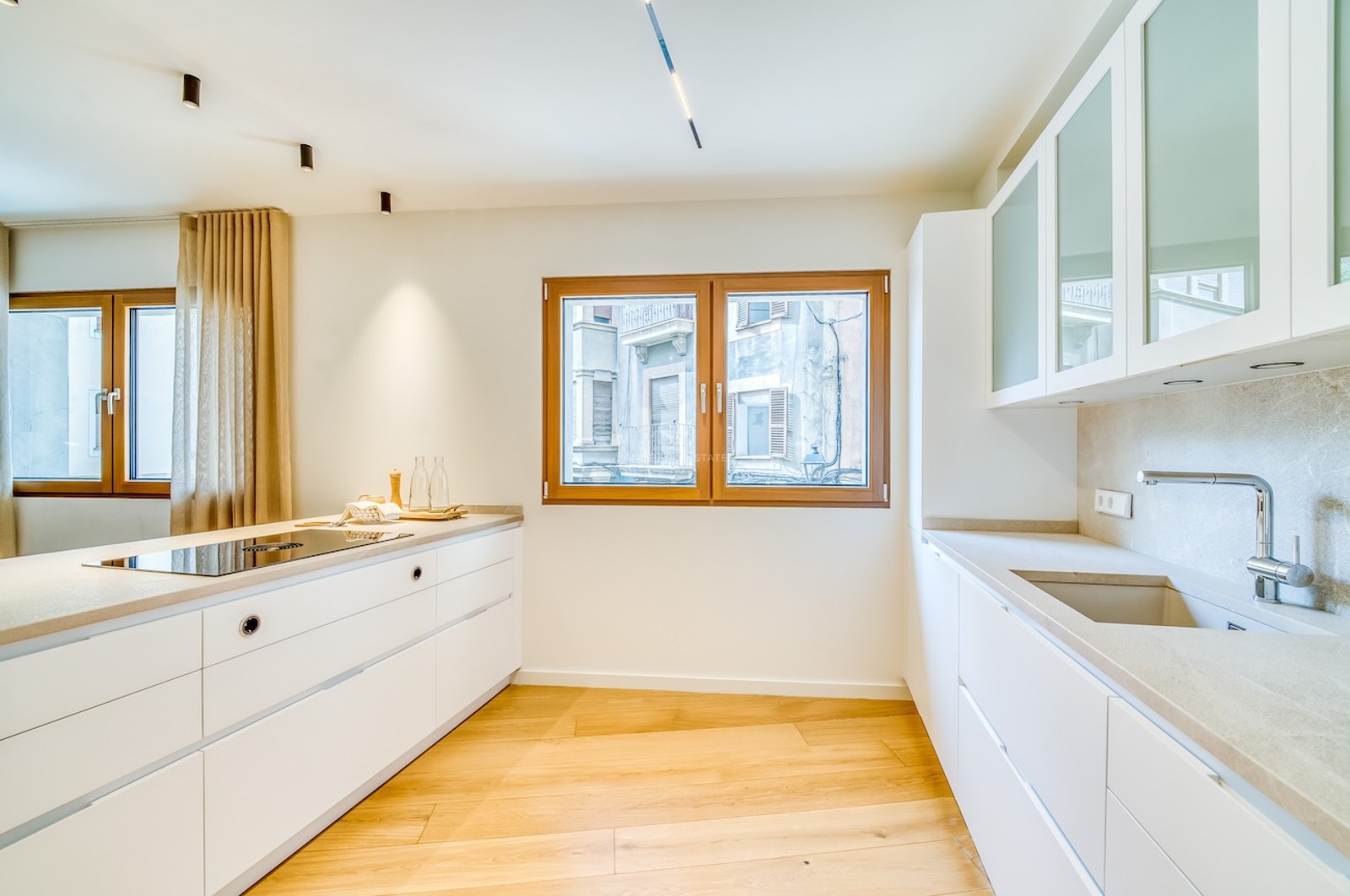 Cuisine blanche moderne avec parquet en chêne, plans de travail en quartz et fenêtres en bois.