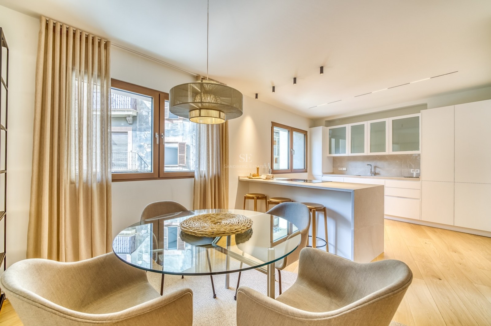 Cuisine moderne ouverte avec placards blancs, îlot en bois avec tabourets et table à manger ronde en verre.