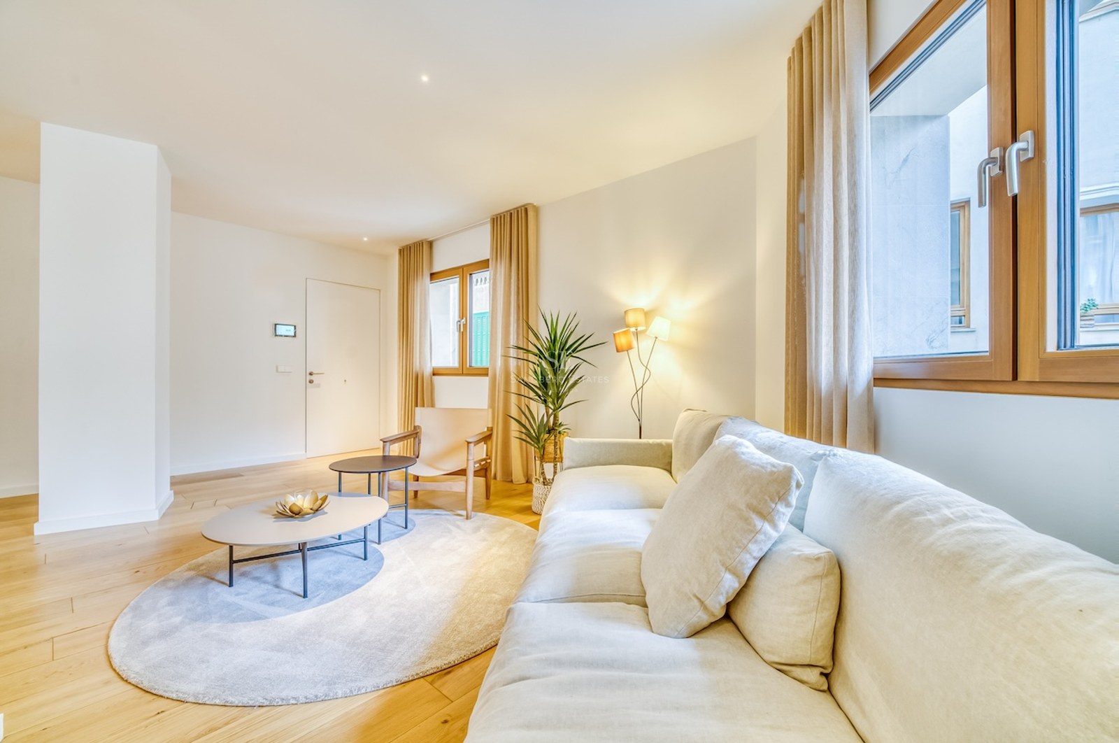 Salon lumineux avec canapé en lin blanc, parquet en chêne, cadres de fenêtres en bois et éclairage chaleureux.