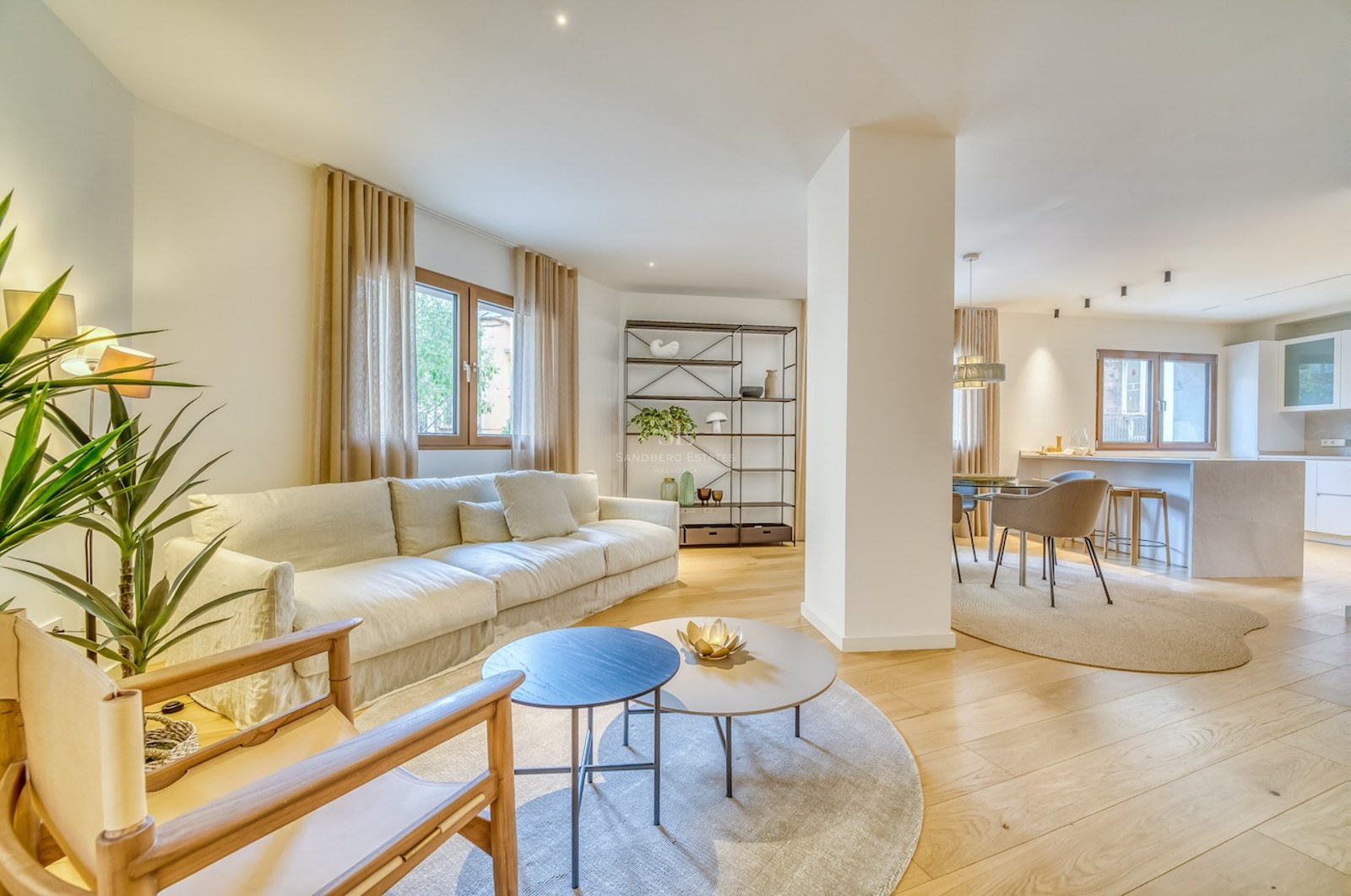 Salon lumineux à aire ouverte avec parquet en chêne clair, canapé crème et espaces cuisine et salle à manger intégrés.