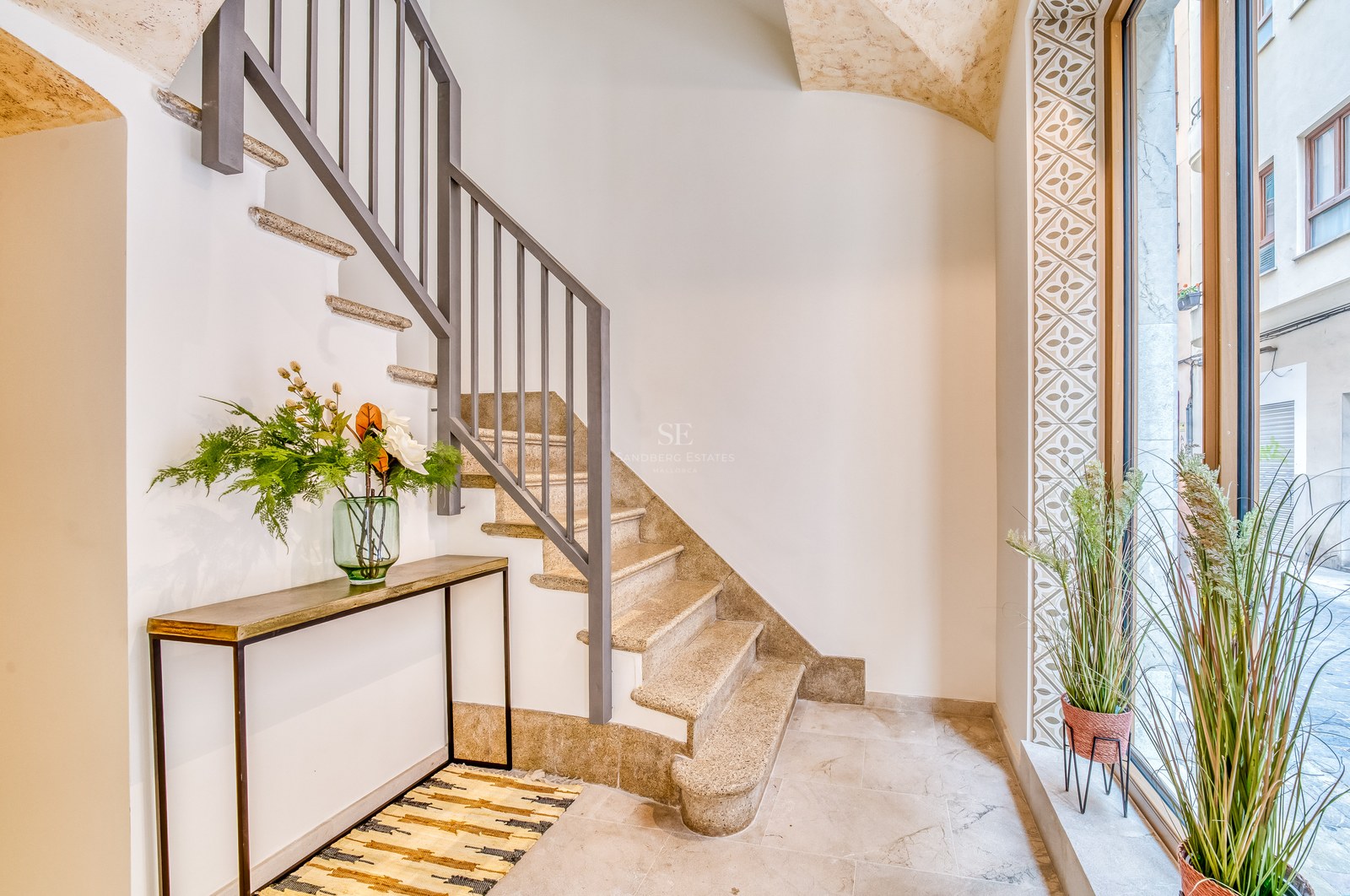 Escalier moderne en pierre avec rampe grise à côté d'une grande fenêtre et d'une console décorative.