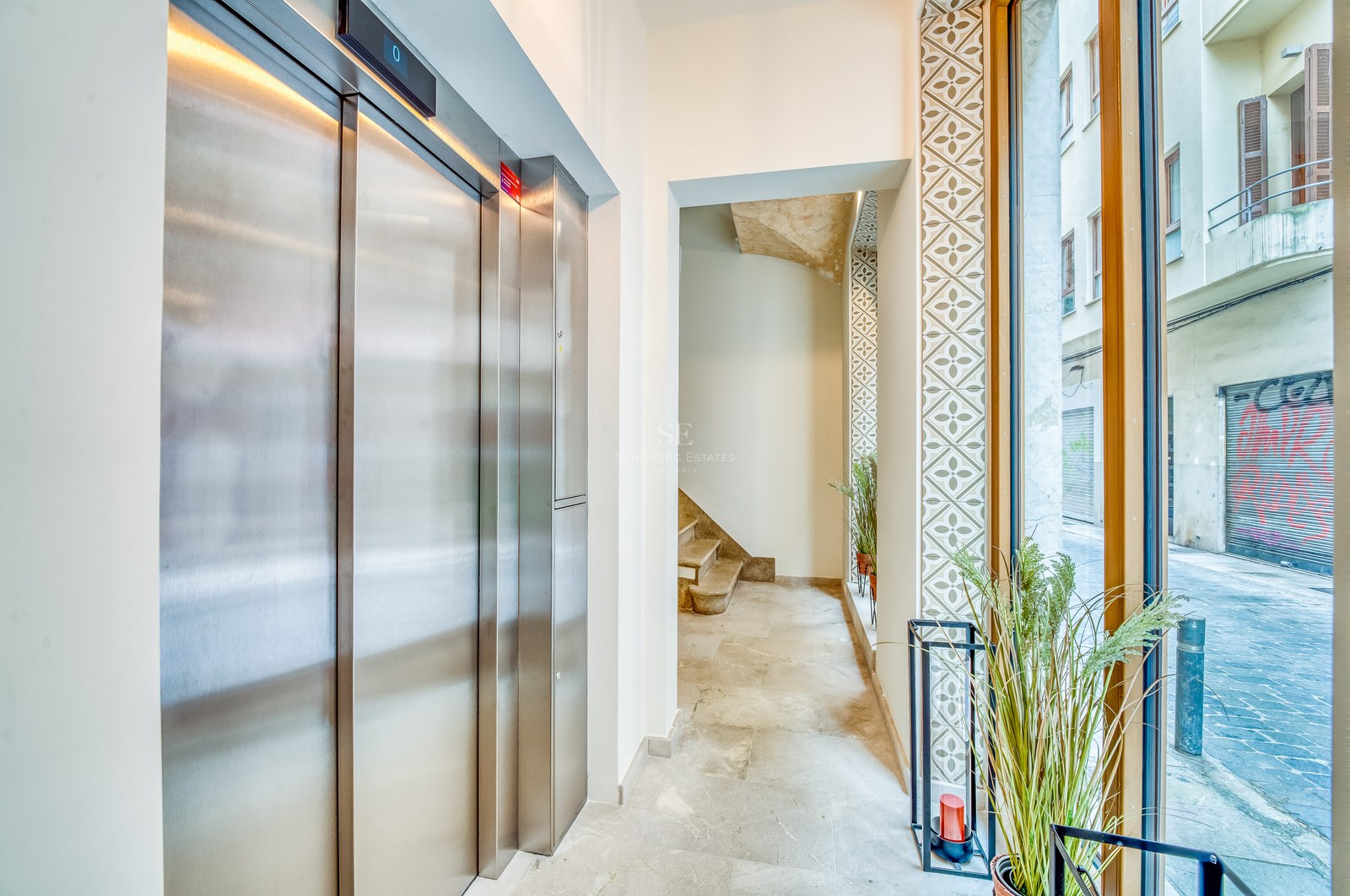 Entrée moderne avec ascenseur en acier inoxydable, sol en pierre naturelle et grande baie vitrée donnant sur la rue.