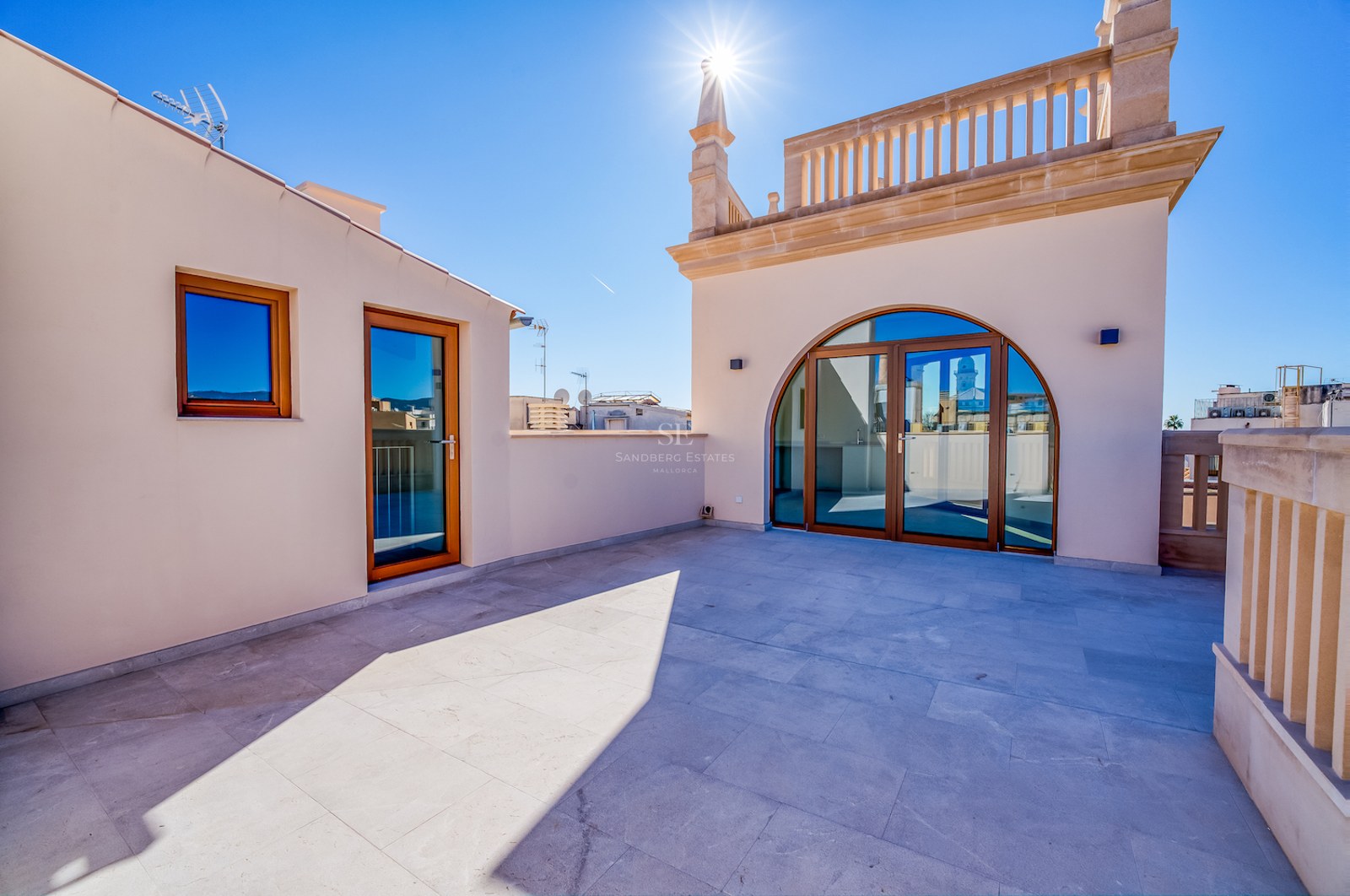 Grande terrasse sur le toit avec dallage en pierre et portes vitrées cintrées sous un ciel bleu azur.