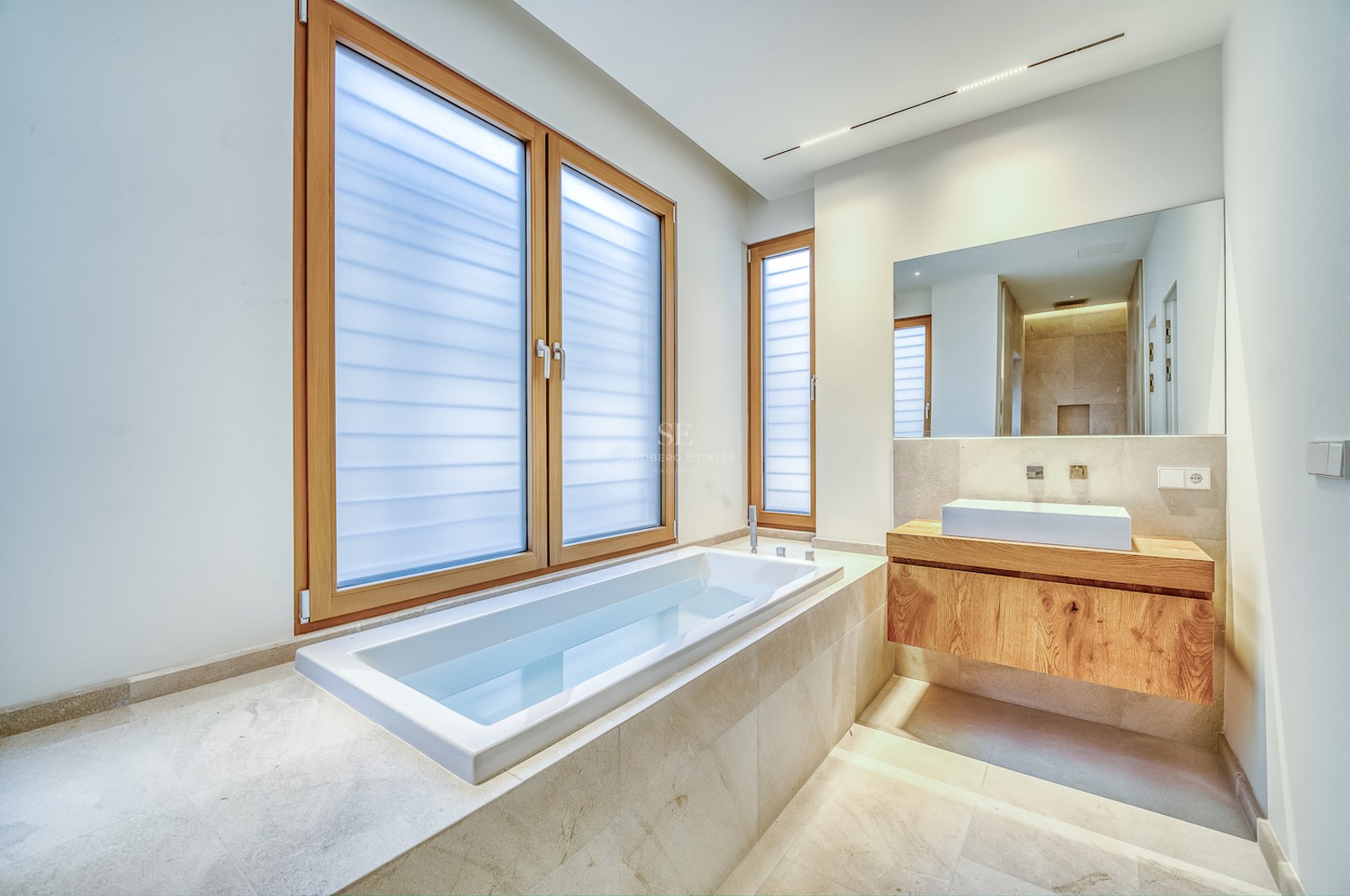 Salle de bains moderne avec baignoire encastrée, meuble vasque en chêne et grandes fenêtres.