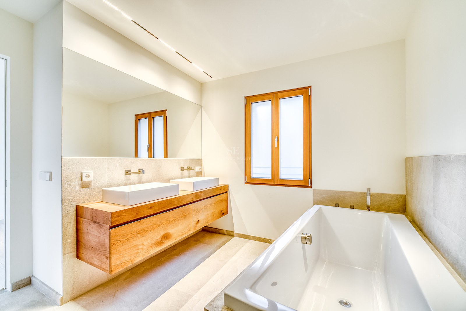 Salle de bains de luxe avec meuble en bois flottant, double vasque, grand miroir et baignoire encastrée.