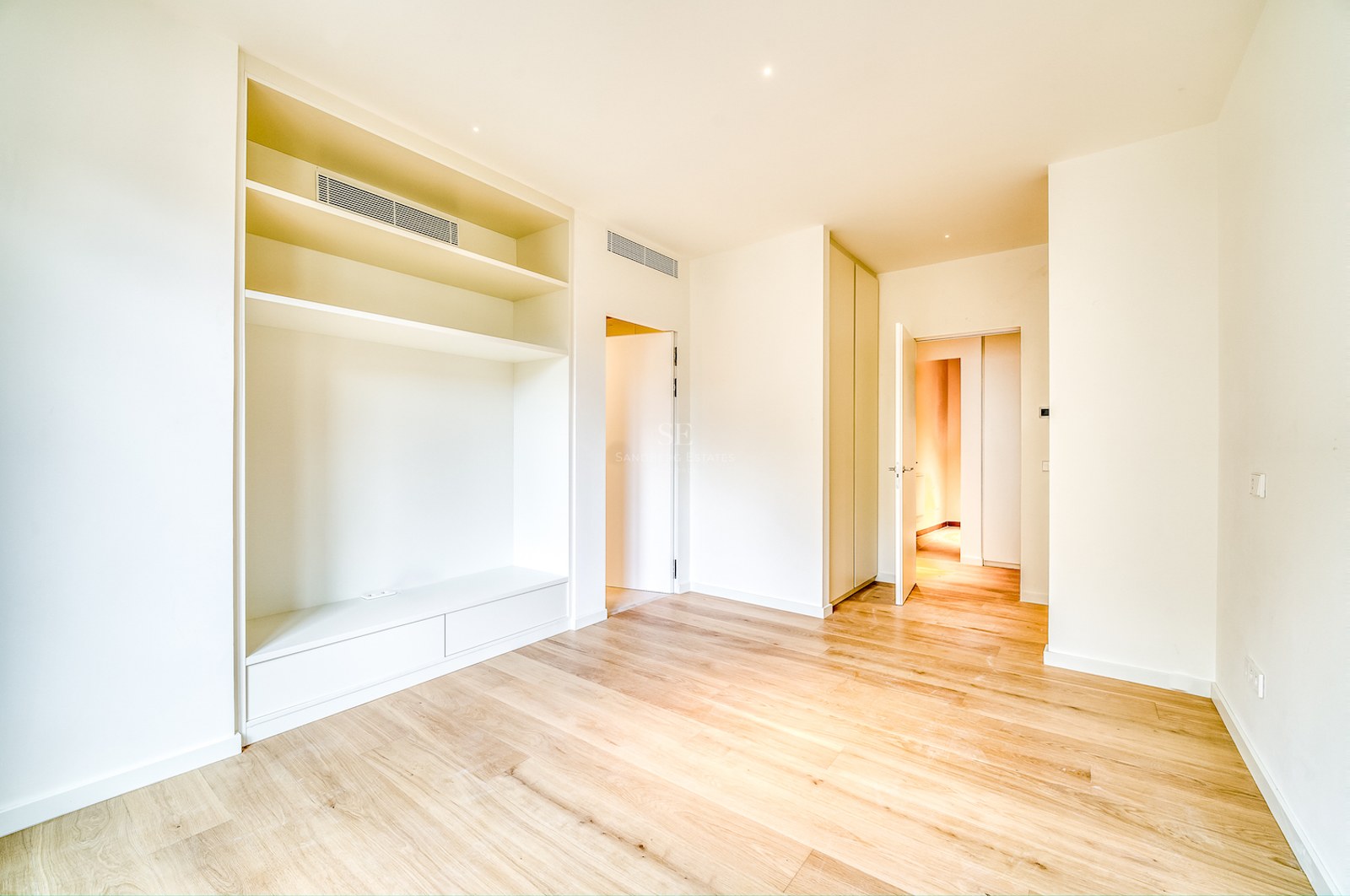 Chambre lumineuse vide avec parquet en chêne clair, étagère blanche sur mesure et placards intégrés.