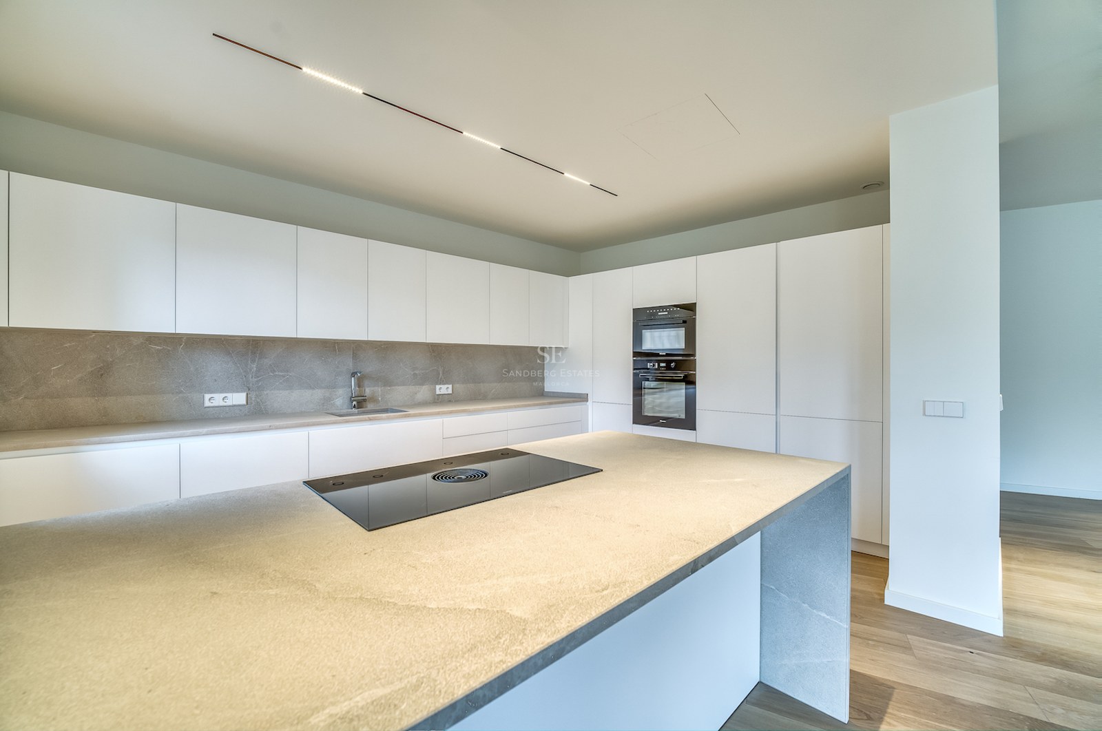 Cuisine moderne avec placards blancs mats, plans de travail en pierre grise et îlot avec plaque de cuisson intégrée.